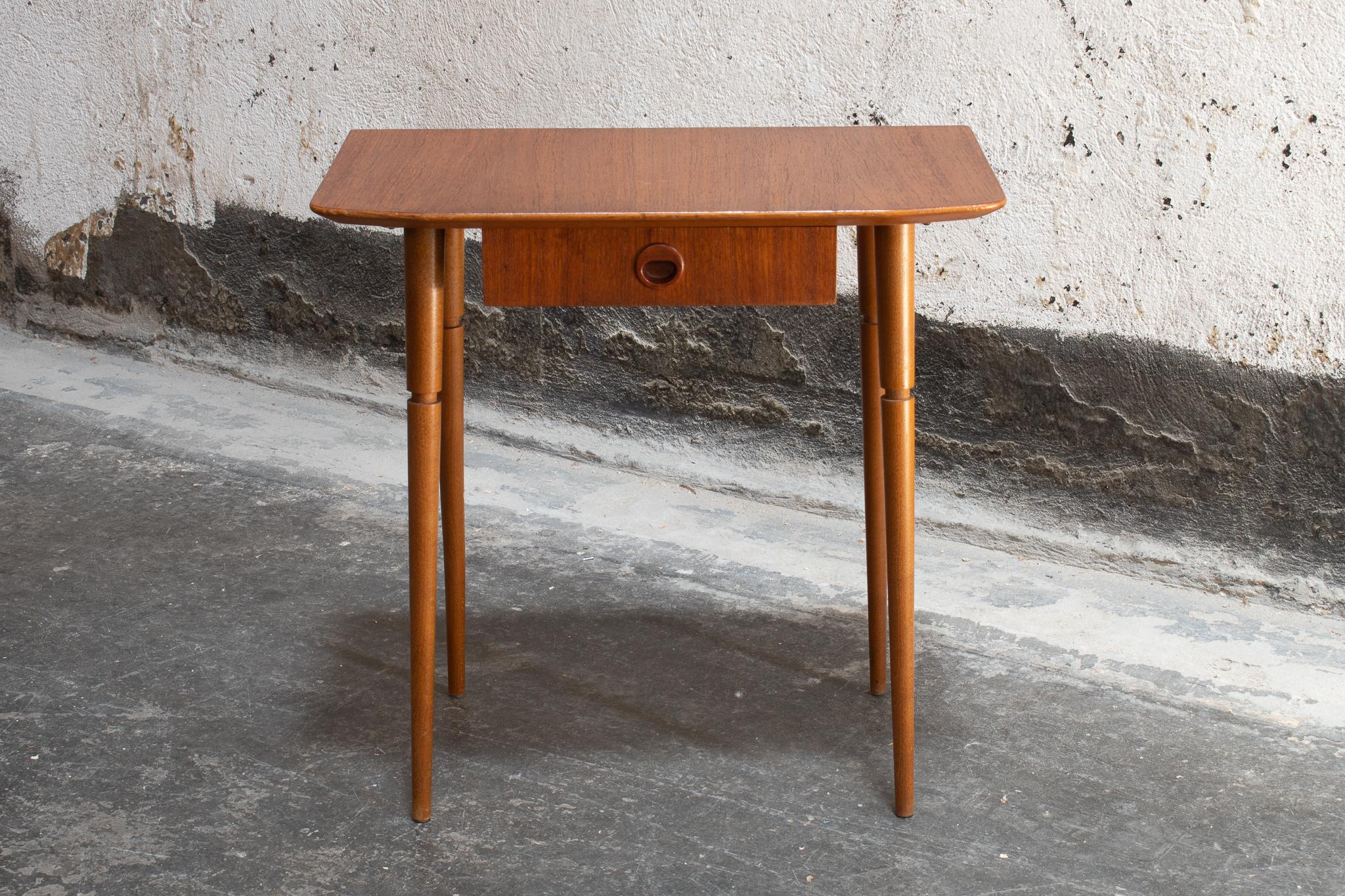 Mid Century Modern nightstand from Sweden, circa 1960. This Scandinavian teak side table has a slight curve at the edge of the tabletop, turned tapered legs, and a small drawer with a mid-mod pull. This Swedish Modern table is perfectly sized for