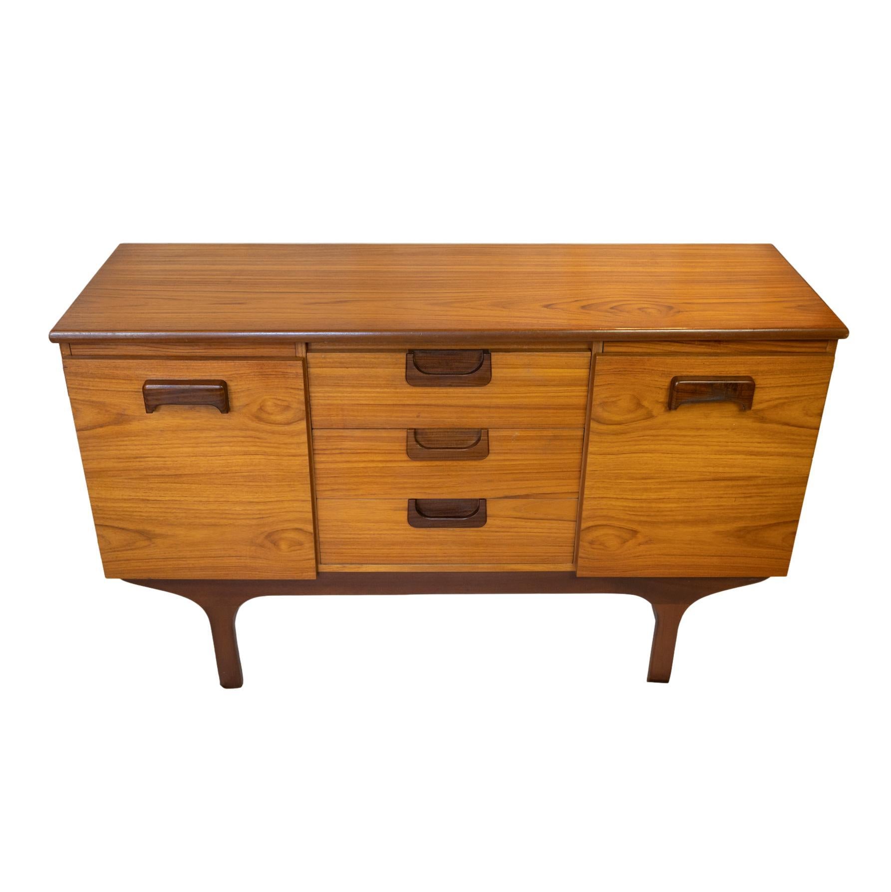 Mid-Century Modern Teak Sideboard by G-Plan, English, circa 1965, the grain-matched case with three central drawers, one fitted for cutlery, with cabinet doors to either side, all with molded sculptural handles, on Danish Modern legs. The top