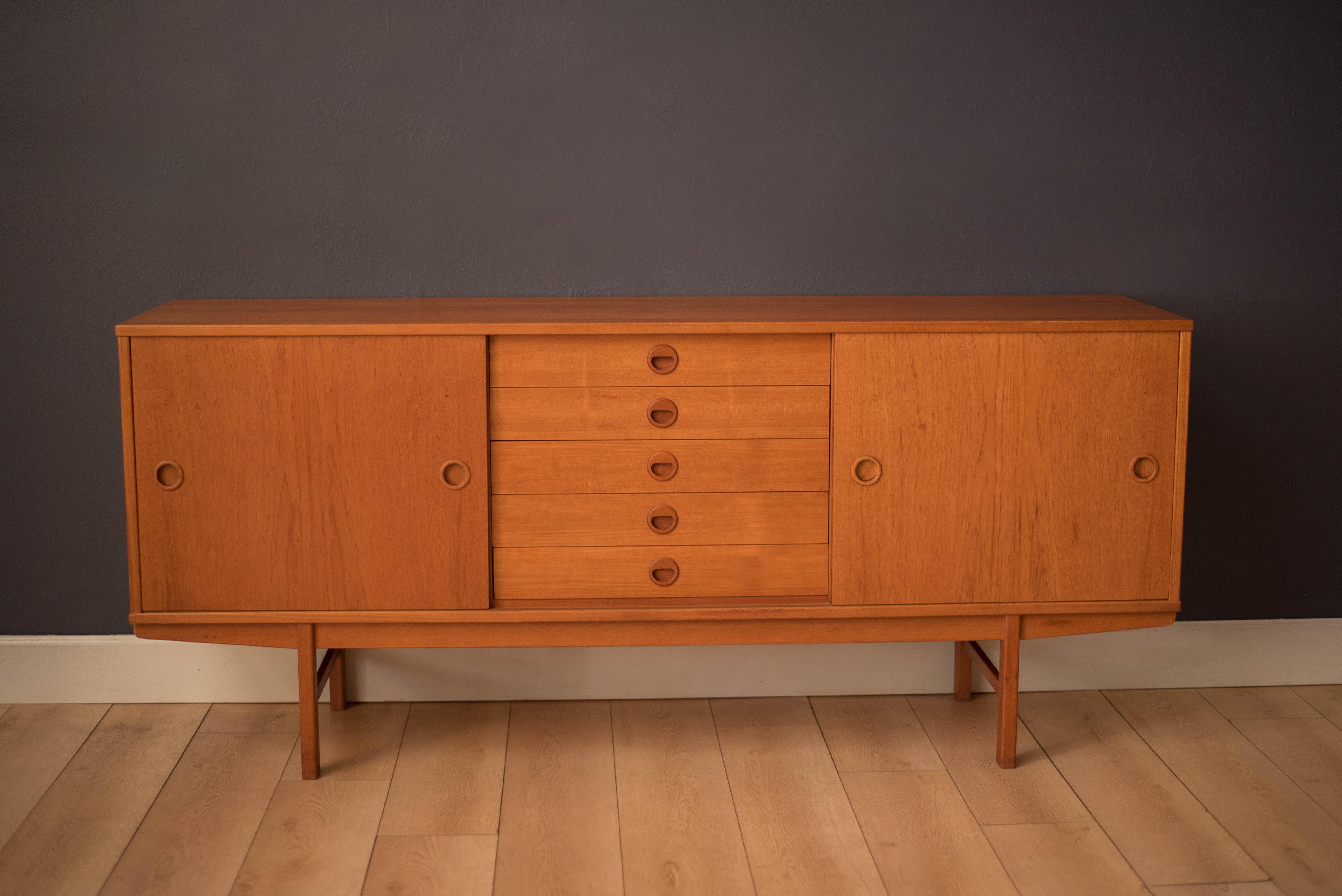 Mid-Century Modern sideboard in teak manufactured by Dux of Sweden, circa 1960s. This piece features convenient sliding doors that display a natural vertical grain pattern with sculpted signature pulls. Offers plenty of storage including five
