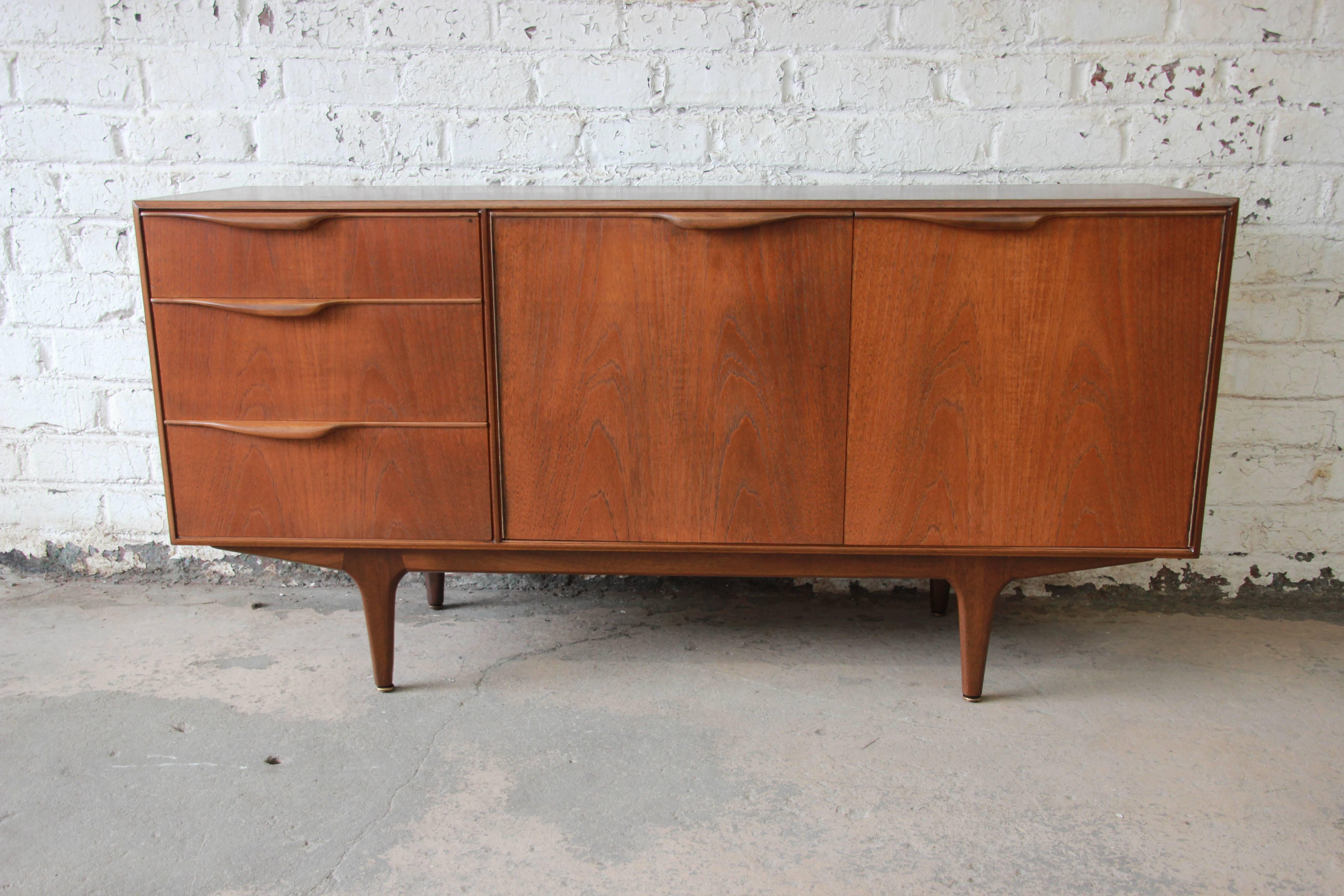 A newly refinished Danish modern style teak sideboard credenza designed by Tom Robertson for A.H. McIntosh. The sideboard features gorgeous teak wood grain and sleek mid-century modern design, with sculpted solid teak drawer pulls. It offers ample