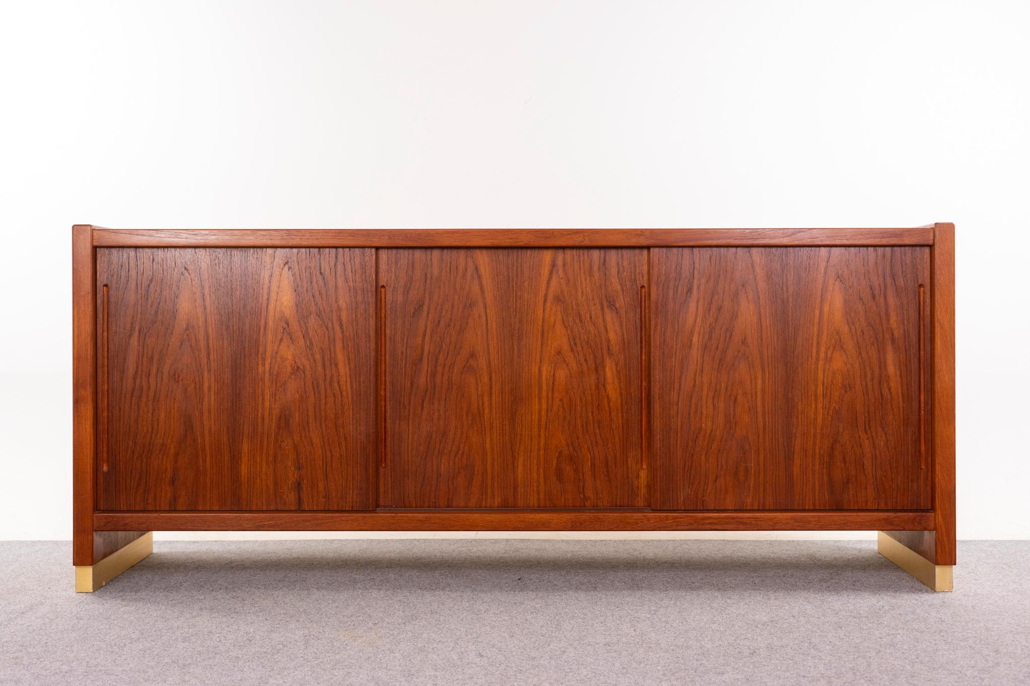 Teak mid-century sideboard, circa 1960s. This robust, substantial sideboard is constructed with bookmatched veneer and solid teak sides, with a brushed metal trim base. It has four height-adjustable shelves.