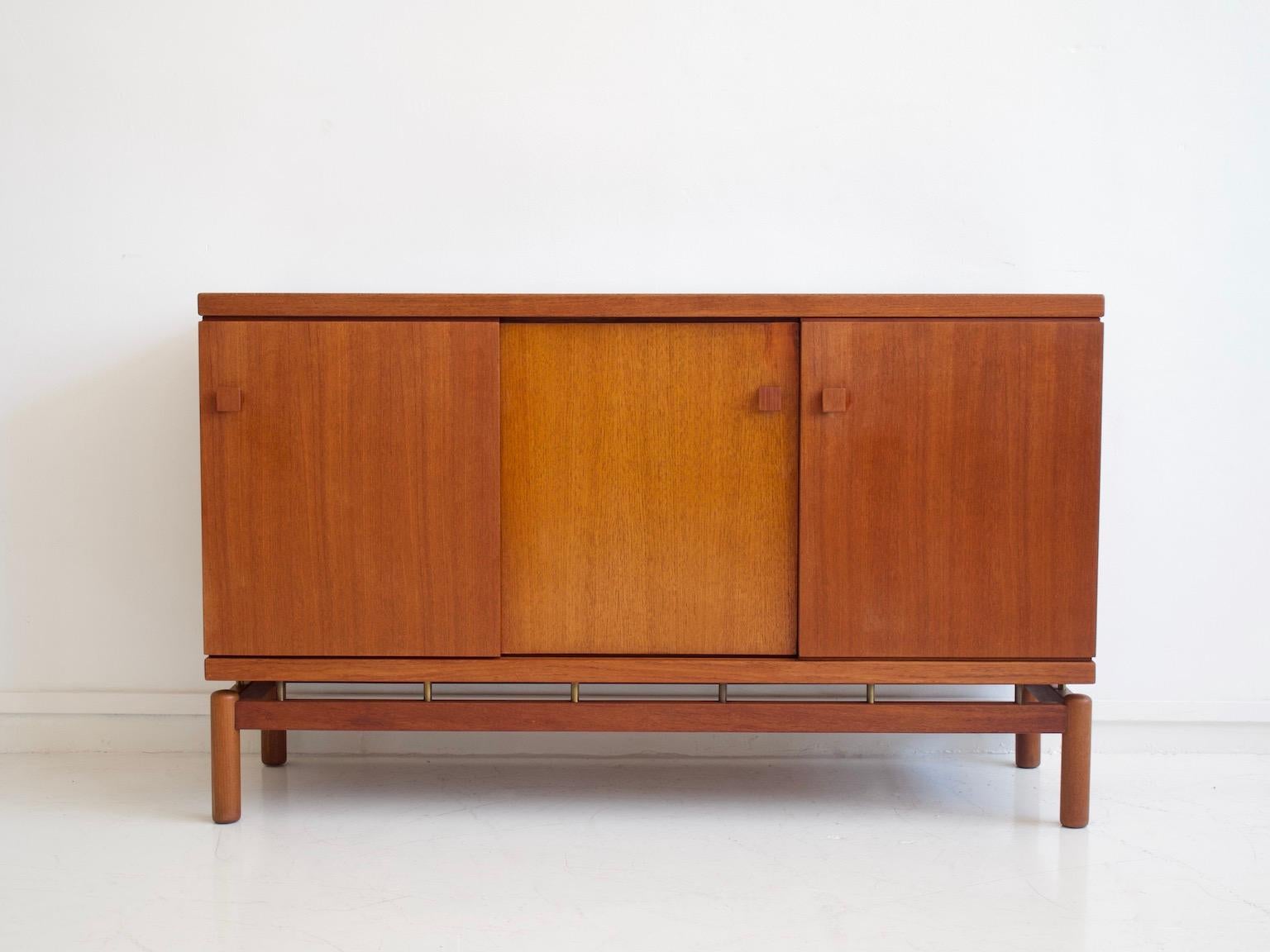 Credenza in legno di teak con ante scorrevoli e dettagli in ottone. I dettagli in ottone tra il corpo del mobile e i piedi conferiscono alla credenza un aspetto fluttuante. Prodotto ed etichettato da La Permanente Mobili Cantù.