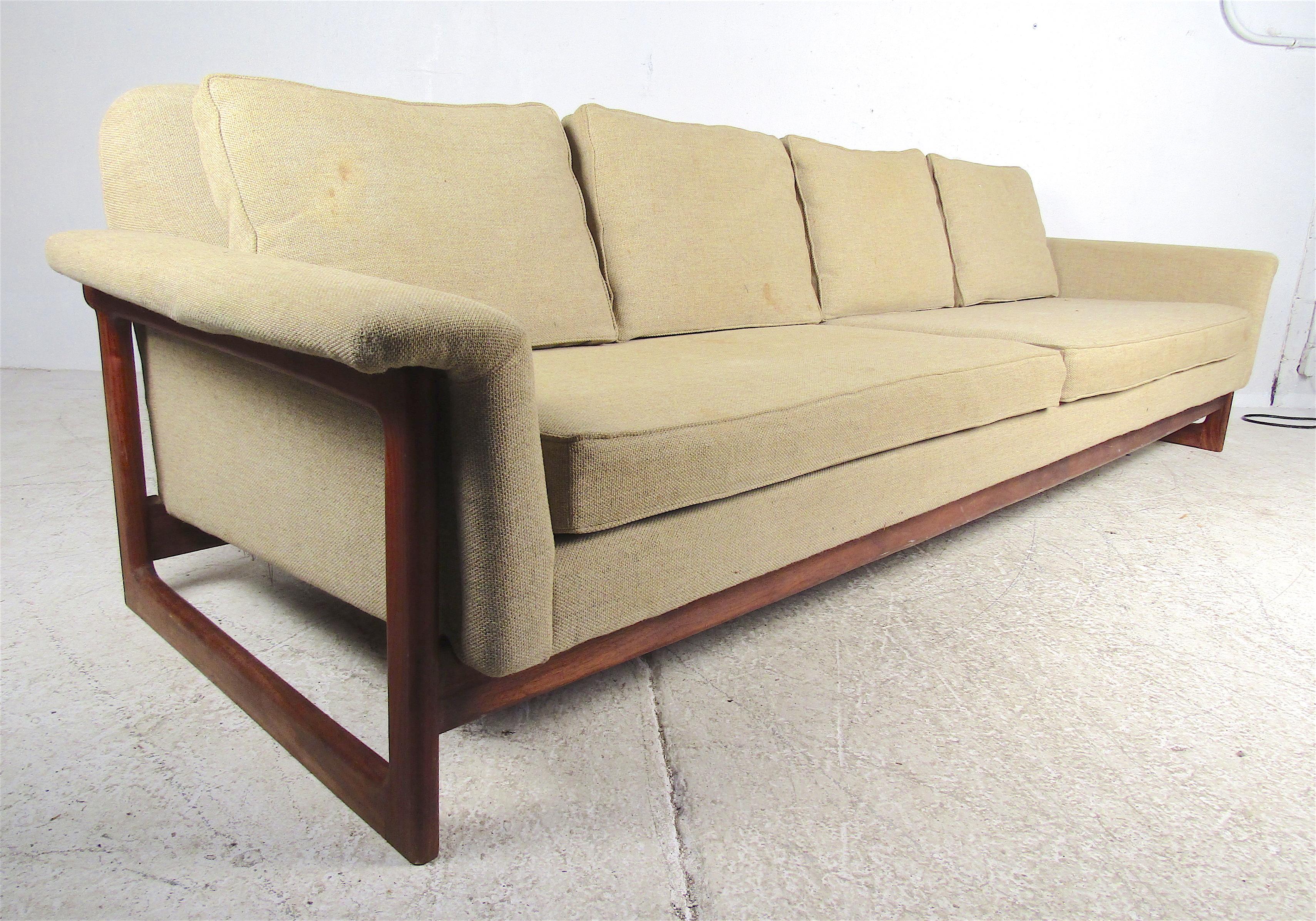 This stunning vintage modern sofa features an exposed solid teak frame with sled legs and winged armrests. A stylish looking sofa that seats three or four easily with overstuffed cushions and four backrests. This sleek and sturdy Danish modern sofa