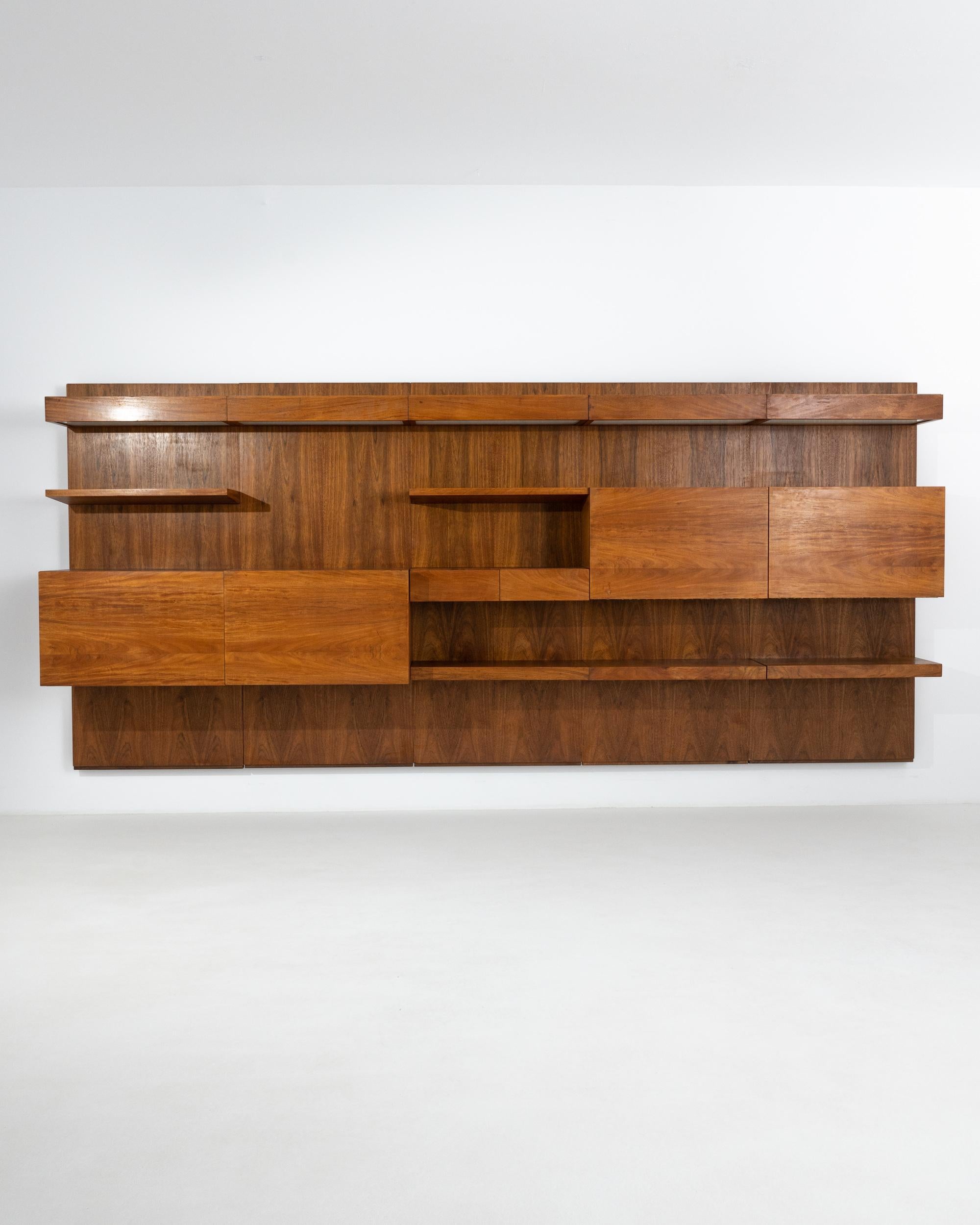 The sleek geometry of linear shelves reveals the fashionable Mid-Century Modern nature of this vintage teak wall unit. Made in the 1960s in Central Europe, this stylish cupboard features a set of open bookshelves and spacious compartments with