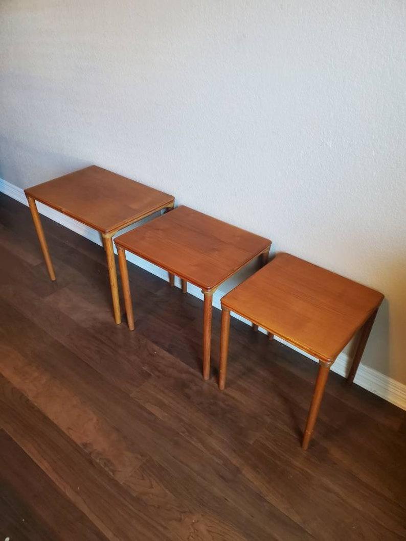 A handsome trio of teak Mid-Century Modern nesting tables. Interlocking, sliding into each other making them sturdy and easy to move around the house. They have the fantastic coloring and elegantly aged fading you expect from vintage teak wood.