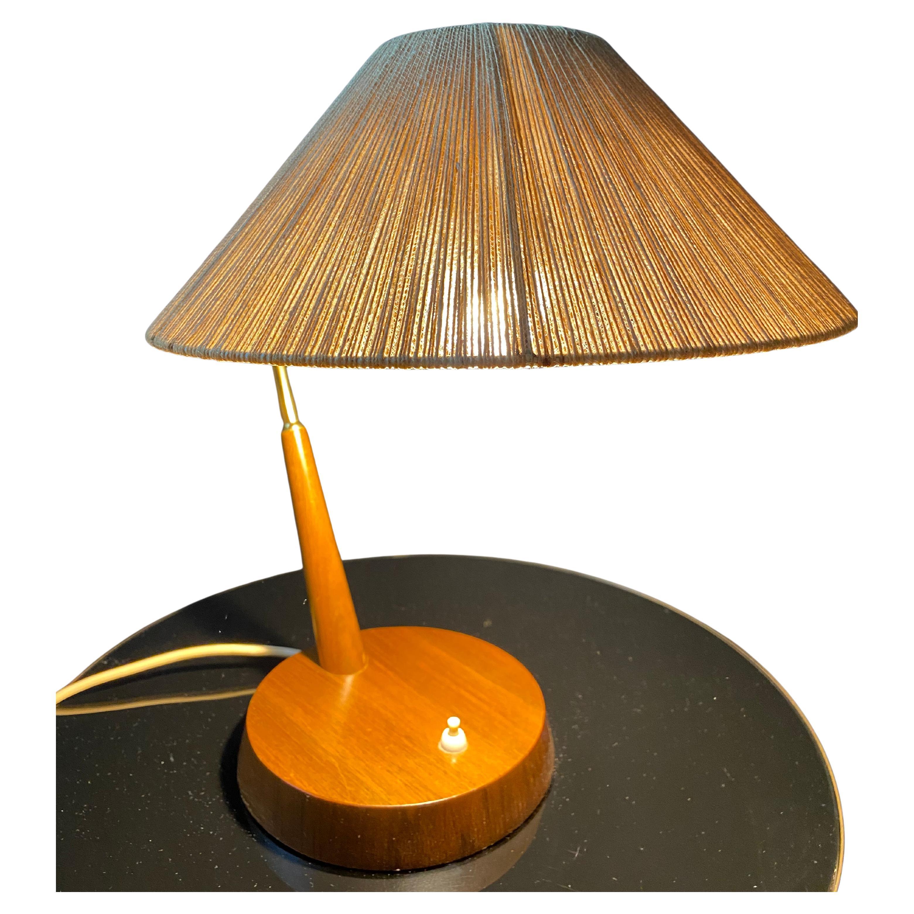 Diese Schreibtischlampe ist der Inbegriff des Mid-Century-Modern-Designs: ein konischer Sisalschirm, ein elegant geformter Messingarm und ein runder Holzsockel mit einem weißen Druckknopfschalter.

Diese Lampe des deutsch-schweizerischen Herstellers