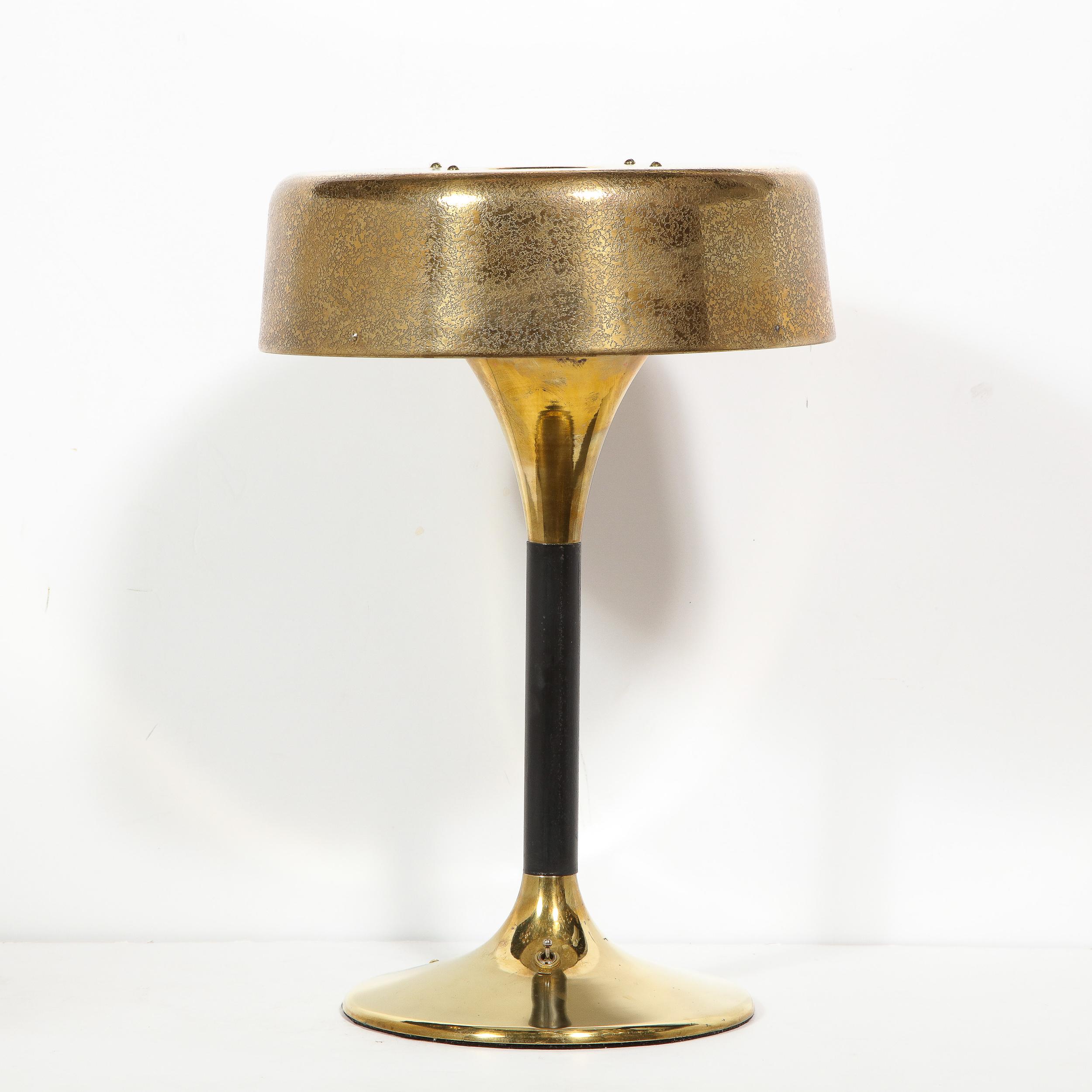 This elegant Mid-Century Modern table lamp was realized in the United States, circa 1950. It features a domed base in polished brass; a cylindrical stem clad in black lacquer; an inverse domed neck in brass; and a volumetric cylindrical shade in