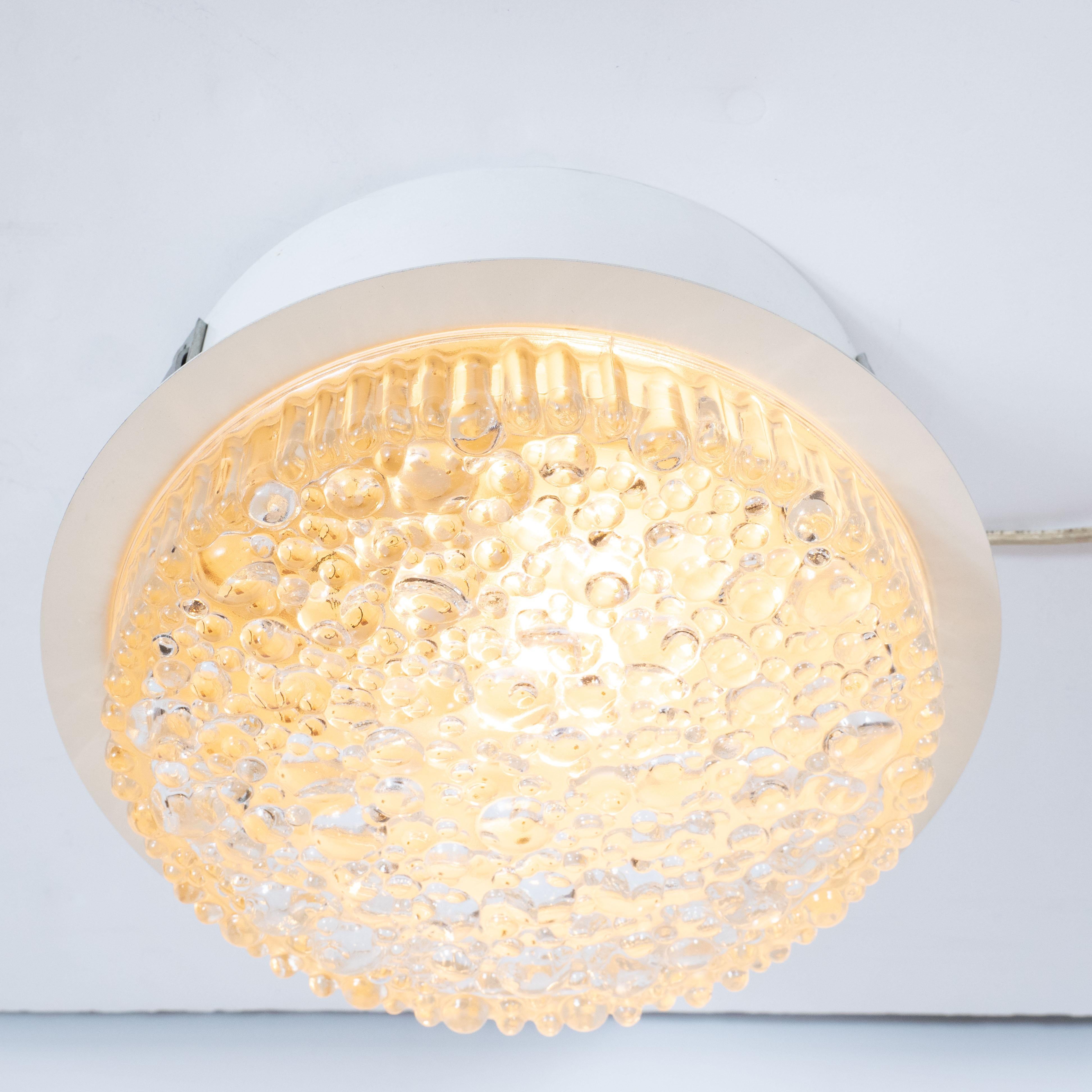 This refined flush mount chandelier was realized in Germany, circa 1960. It features a shallow cylindrical form (intended to be inset into the ceiling) with an abundance of bubbles- raised circular shapes- of varying diameter, lending it a