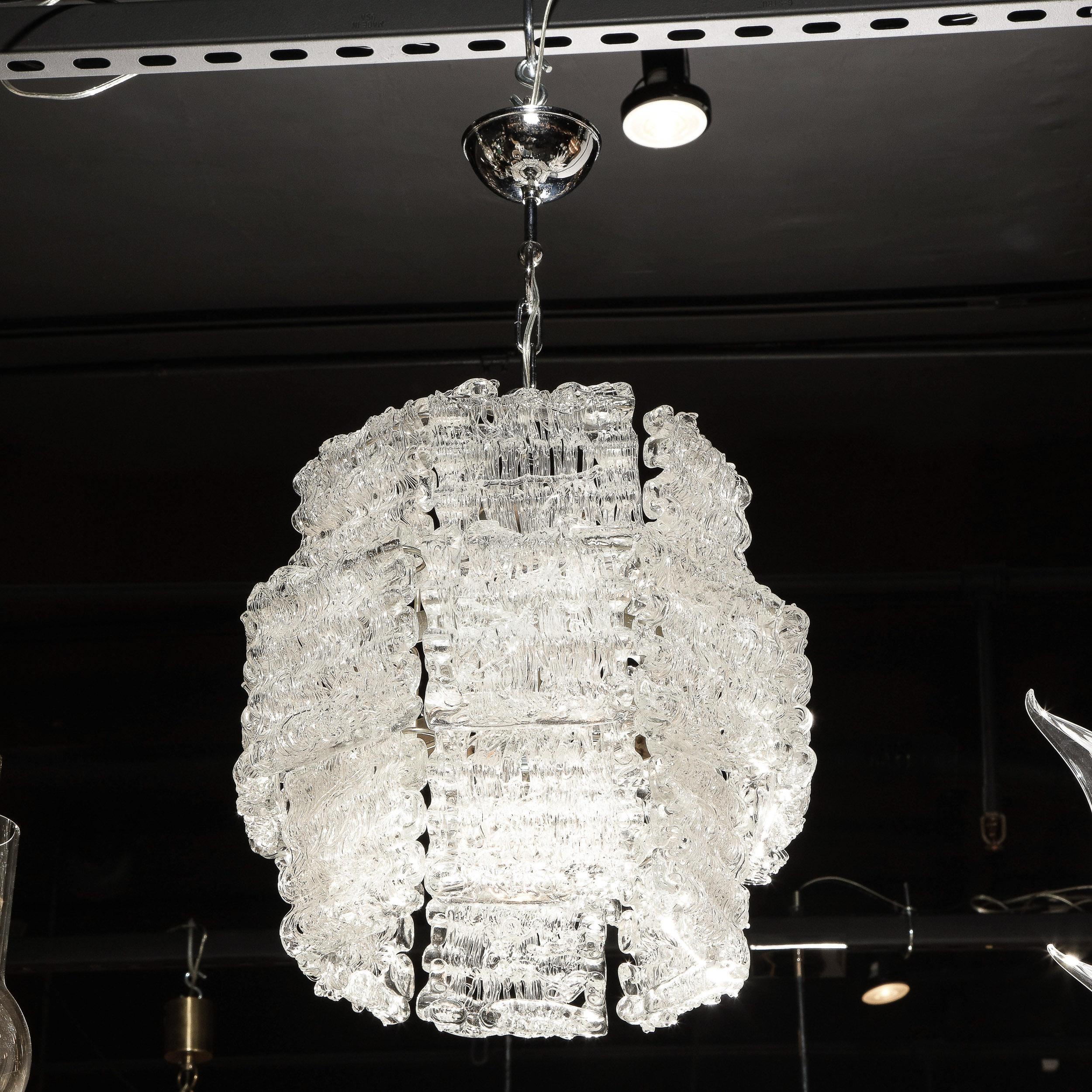 This stunning Mid-Century Modern chandelier was realized in Italy, circa 1970. It features a cylindrical body with a subtly flared center composed of panels of highly textural translucent glass- resembling ice- attached to a chrome frame. With its