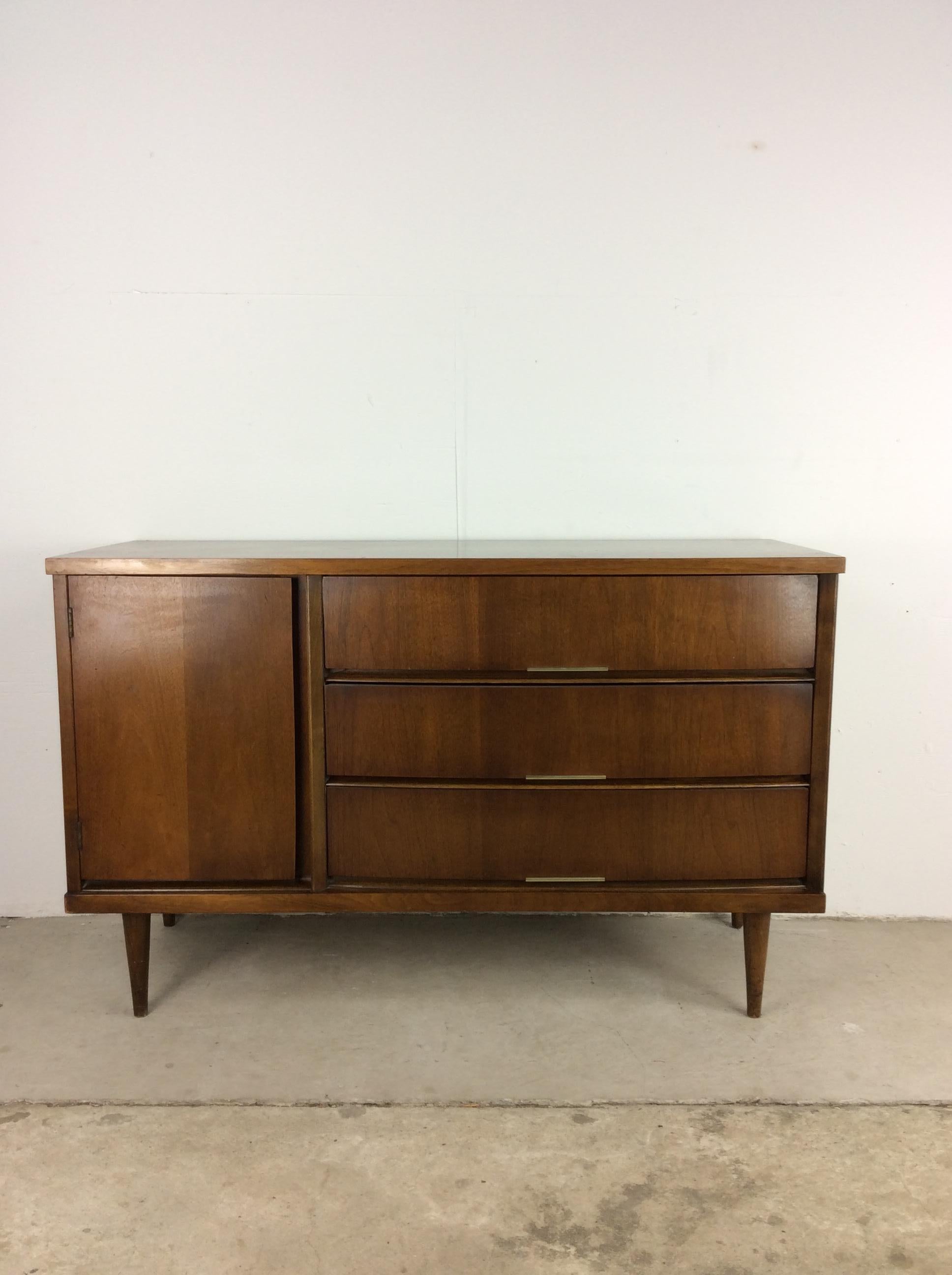 his Mid-Century Modern credenza by Bassett Furniture features hardwood construction, original walnut finish, three dovetailed drawers with inlaid brass accented hardware, one cabinet with single shelf, and tall tapered legs. 

Dimensions: 48w