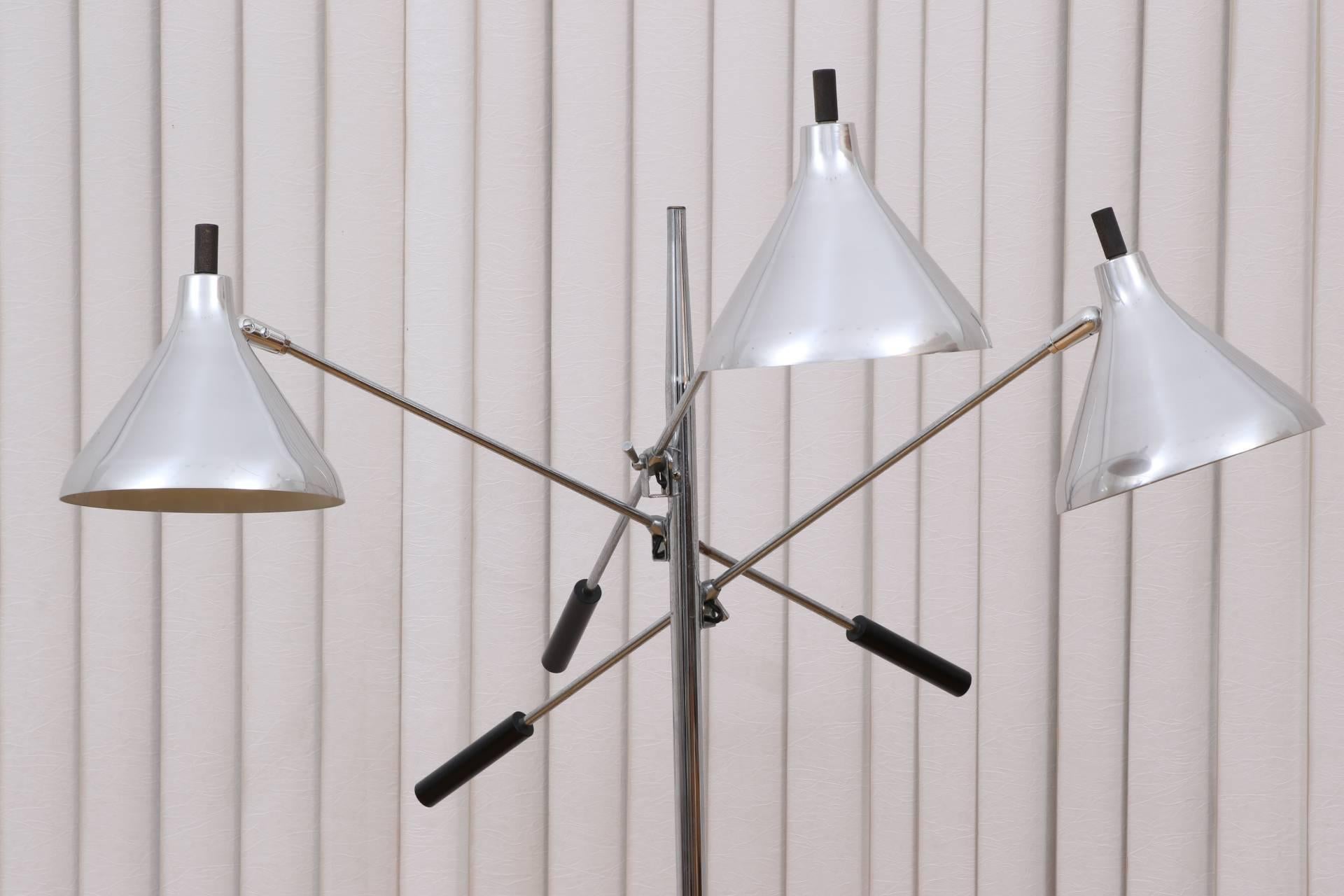 Tall chrome and black metal standard on a black metal round base, with three adjustable long chrome arms with black ends and adjustable aluminium shades with wood finials, circa 1960s. The adjustable knob and light switch on the