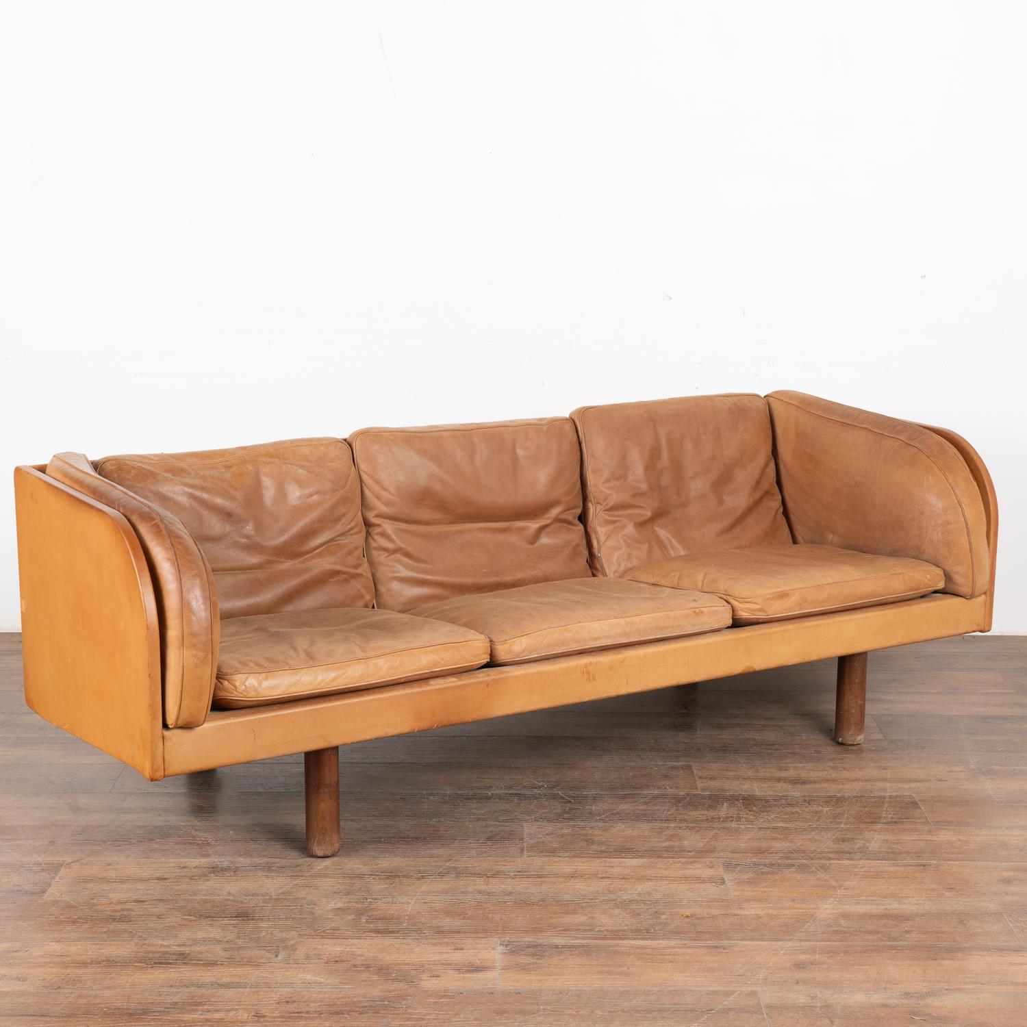 Handsome mid-century modern brown leather three-seat sofa with impressive, curved arms.
The years of use are revealed in the aged patina of the leather, including impressions, scuffs/scratches, stains, discolorations throughout, etc. which all add