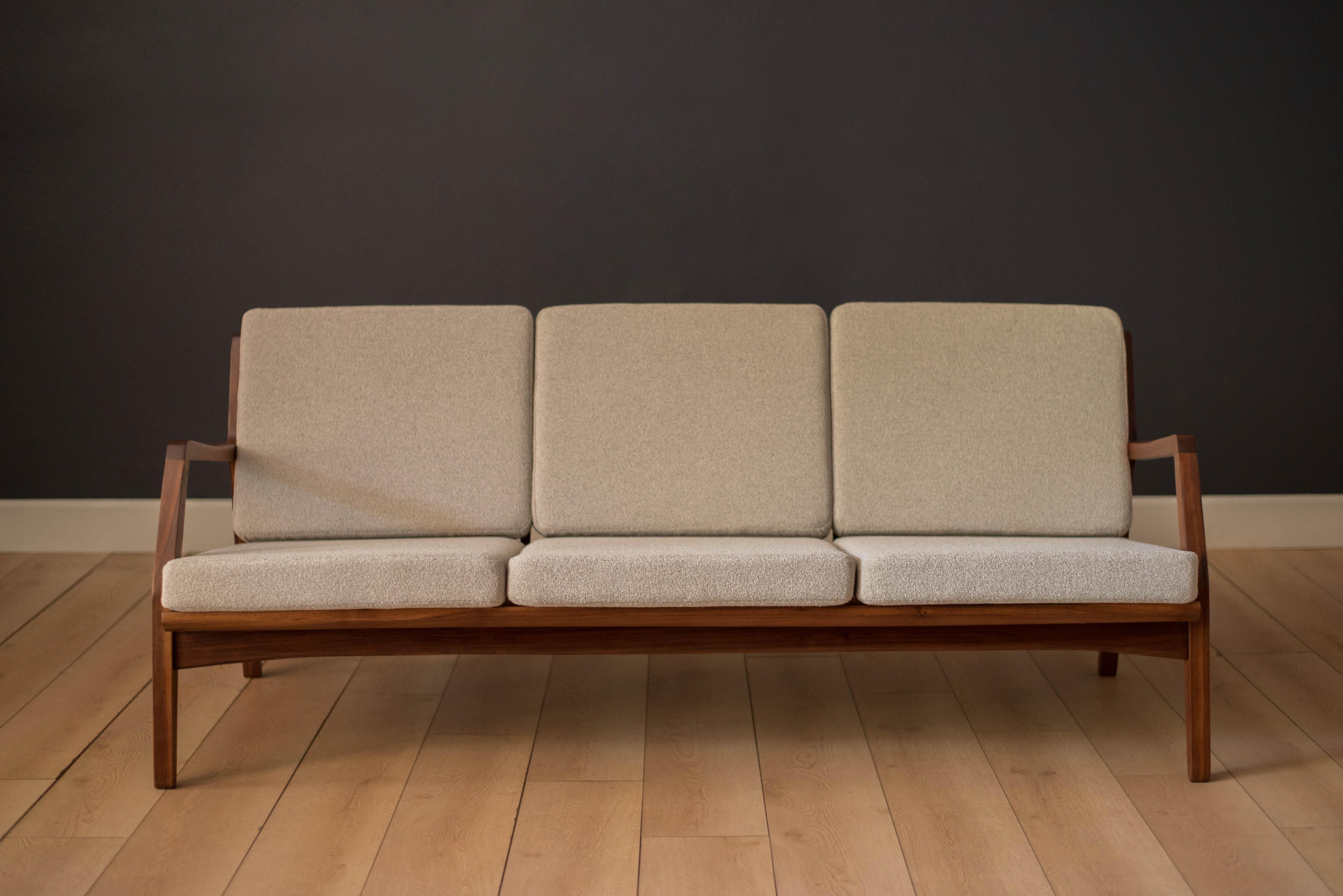 Vintage three-seat sofa constructed of solid walnut, circa 1960s. This piece has been professionally reupholstered in a nubby light grey boucle fabric supported by brand new Pirelli webbing. Features a sculptural walnut frame that can be displayed