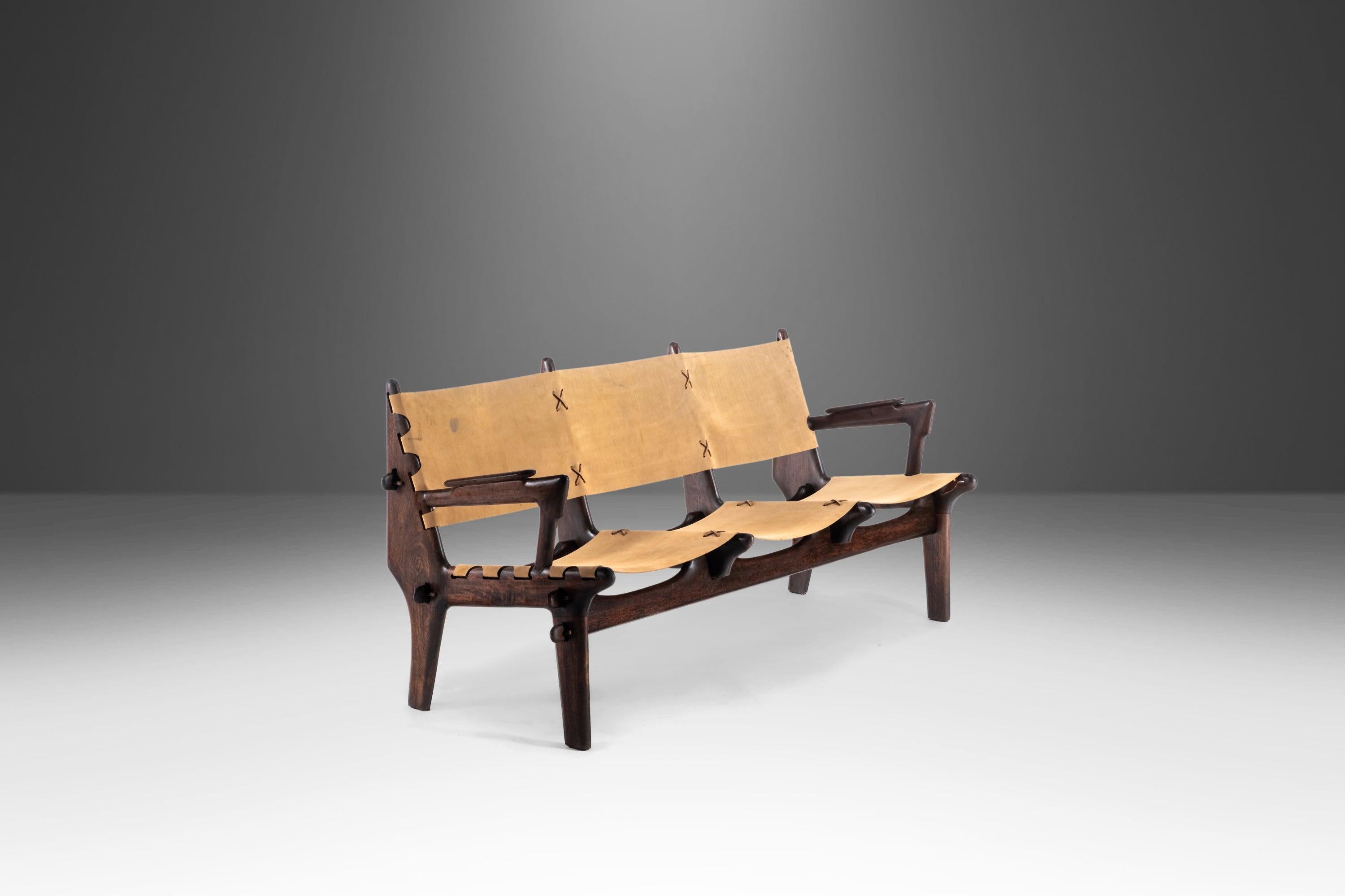 Tan raro como estéticamente cautivador, este sofá de tres plazas asombrosamente único de mediados del siglo XX, obra del ecuatoriano Angel Pazmino, es el epítome del arte funcional. Fabricado por artesanos con maderas duras tropicales y arneses de