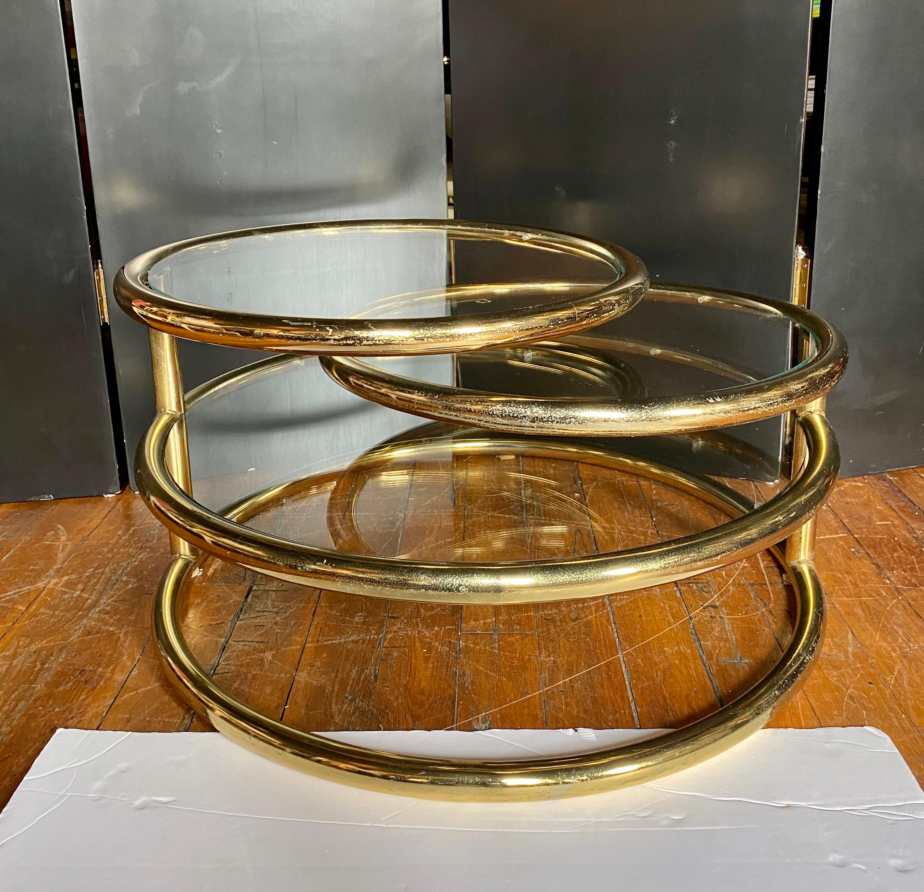 Mid Century Modern three tier brass gold plated metal and glass swivel coffee table in the style of Milo Baughman. The top two tiers of this versatile cocktail table pivot to expand to a width of 71.5 inches when fully extended. This round tubular