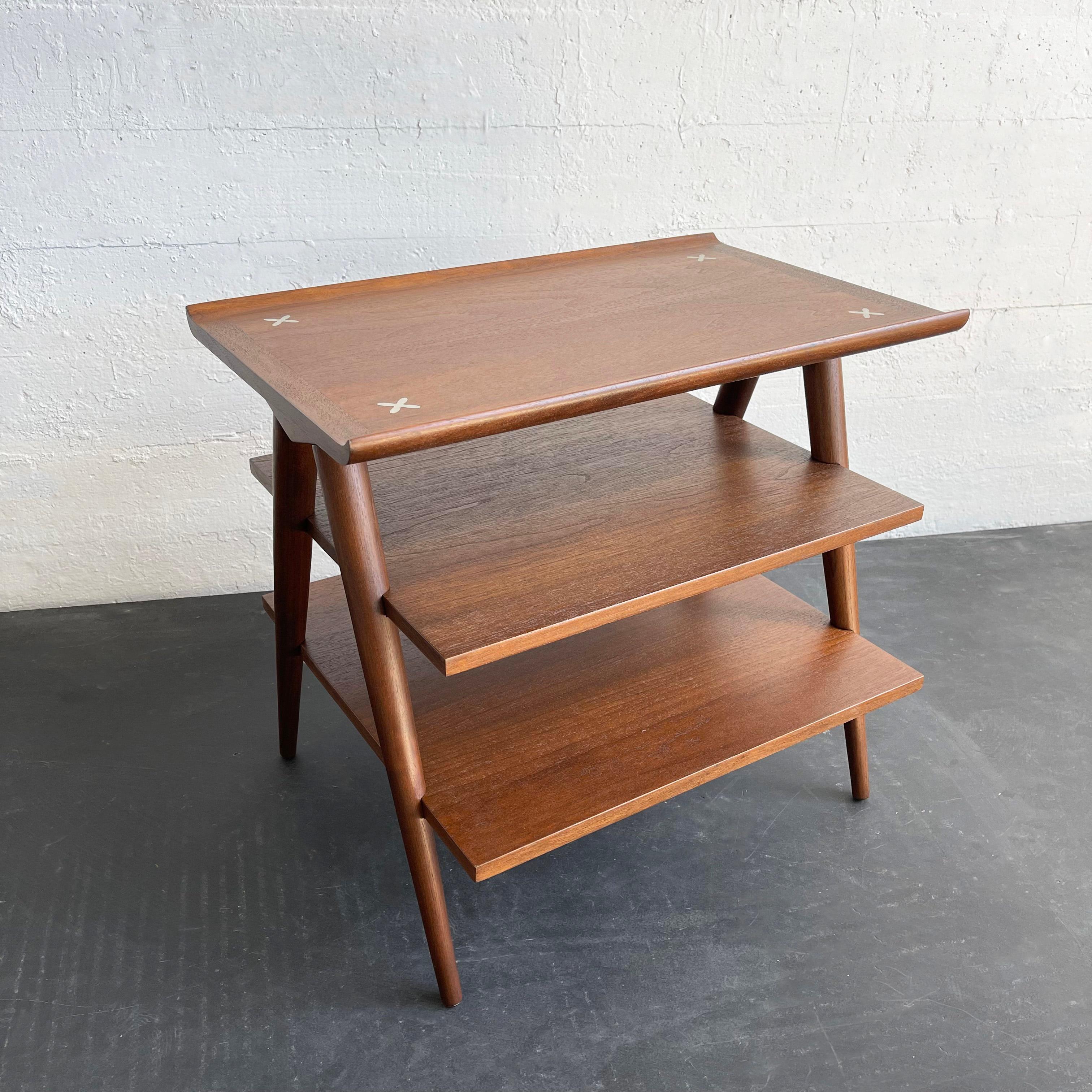 Sleek and sculptural, mid-century modern, walnut side table designed by Merton Gershun for American of Martinsville features slanted, tapered legs that support three tiers perfect for displaying books and magazines. A signature trait of Gershun’s is