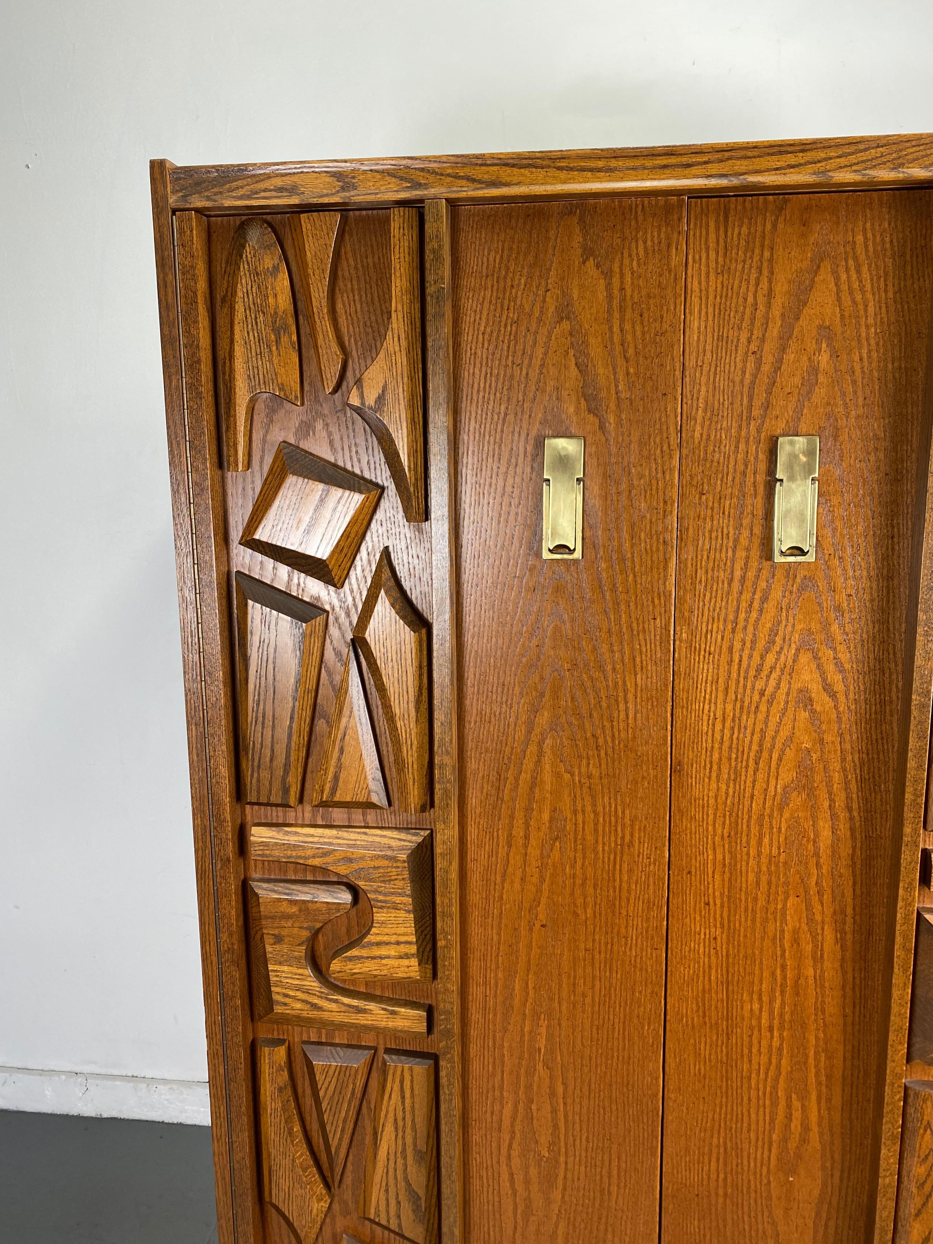 Mid-Century Modern Tiki Brutalist armoire or cabinet. Unusual cabinet featuring sculpted panel doors, four large cubbies and four drawers, handsome brass pull.