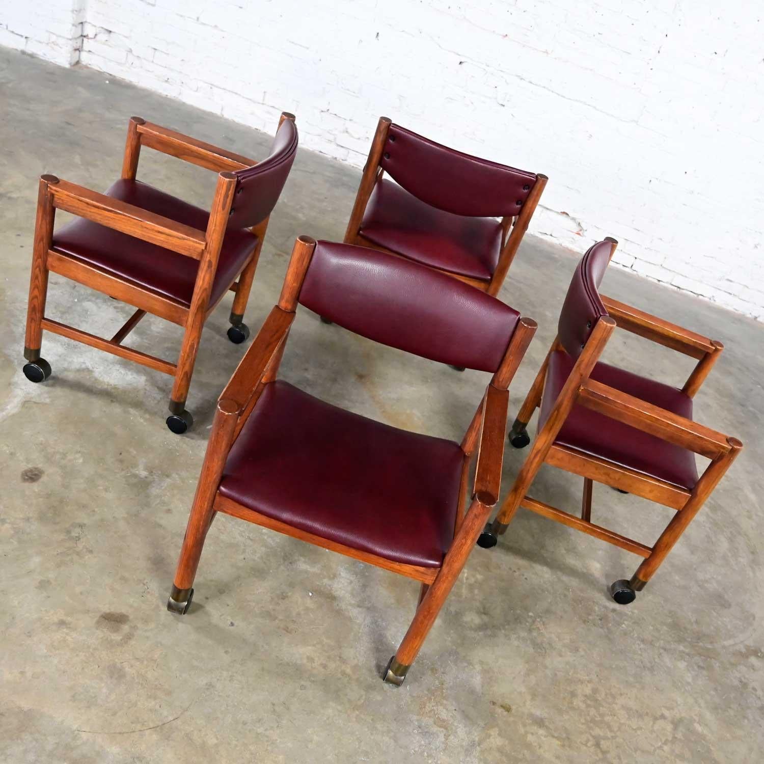 Wonderful Mid-Century Modern to modern rolling game or dining chairs comprised of oak frames, maroon vinyl seats and backs, brass sabots, and casters. Beautiful condition, keeping in mind that this is vintage and not new so will have signs of use