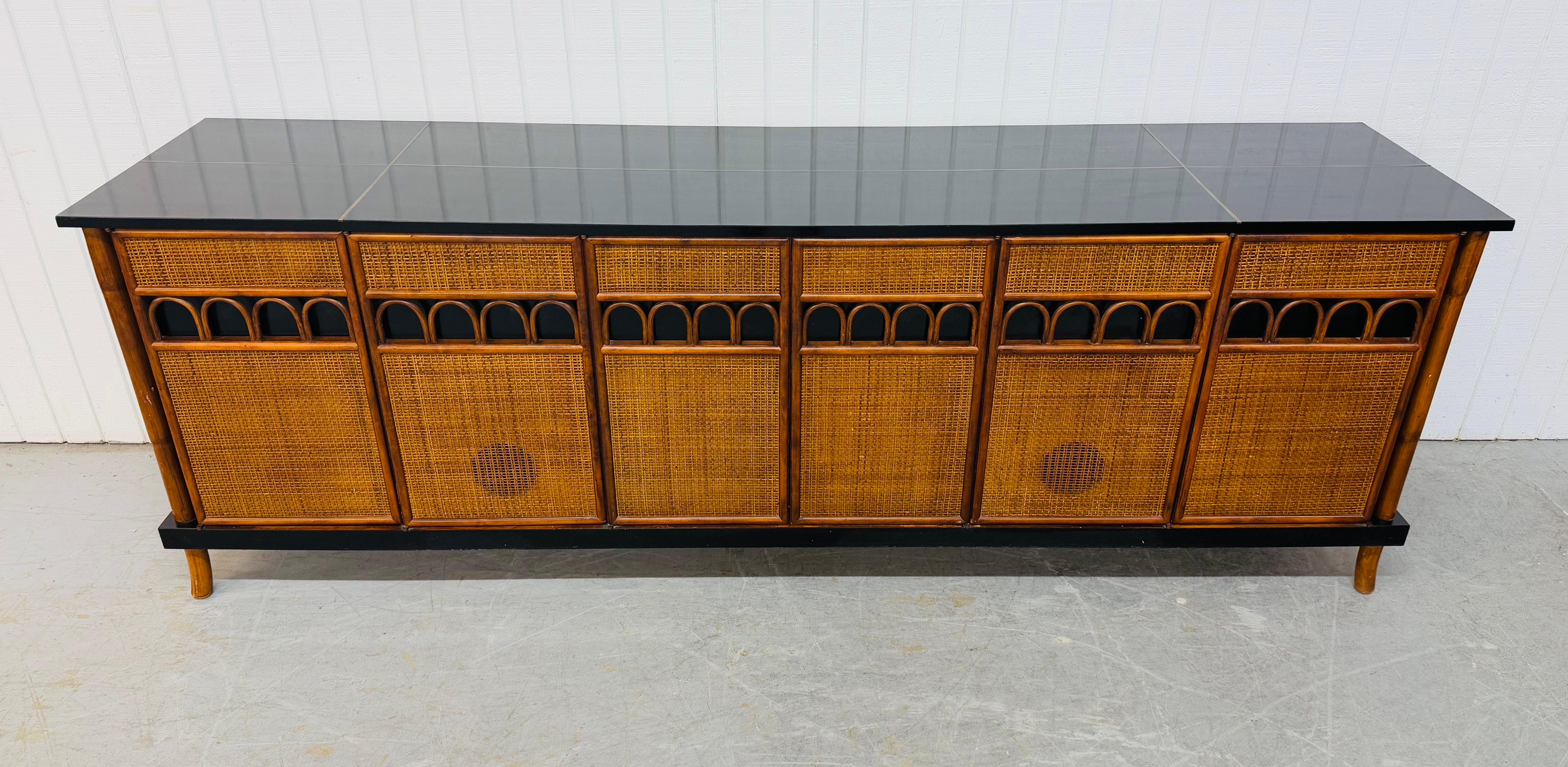 Questo annuncio si riferisce a una credenza in canna di rattan in stile metà secolo moderno di Tommi Parzinger. Design lineare, scomparti multipli, gambe in rattan, facciata/fianchi in canna, piano laccato nero e finitura in noce. Si tratta di