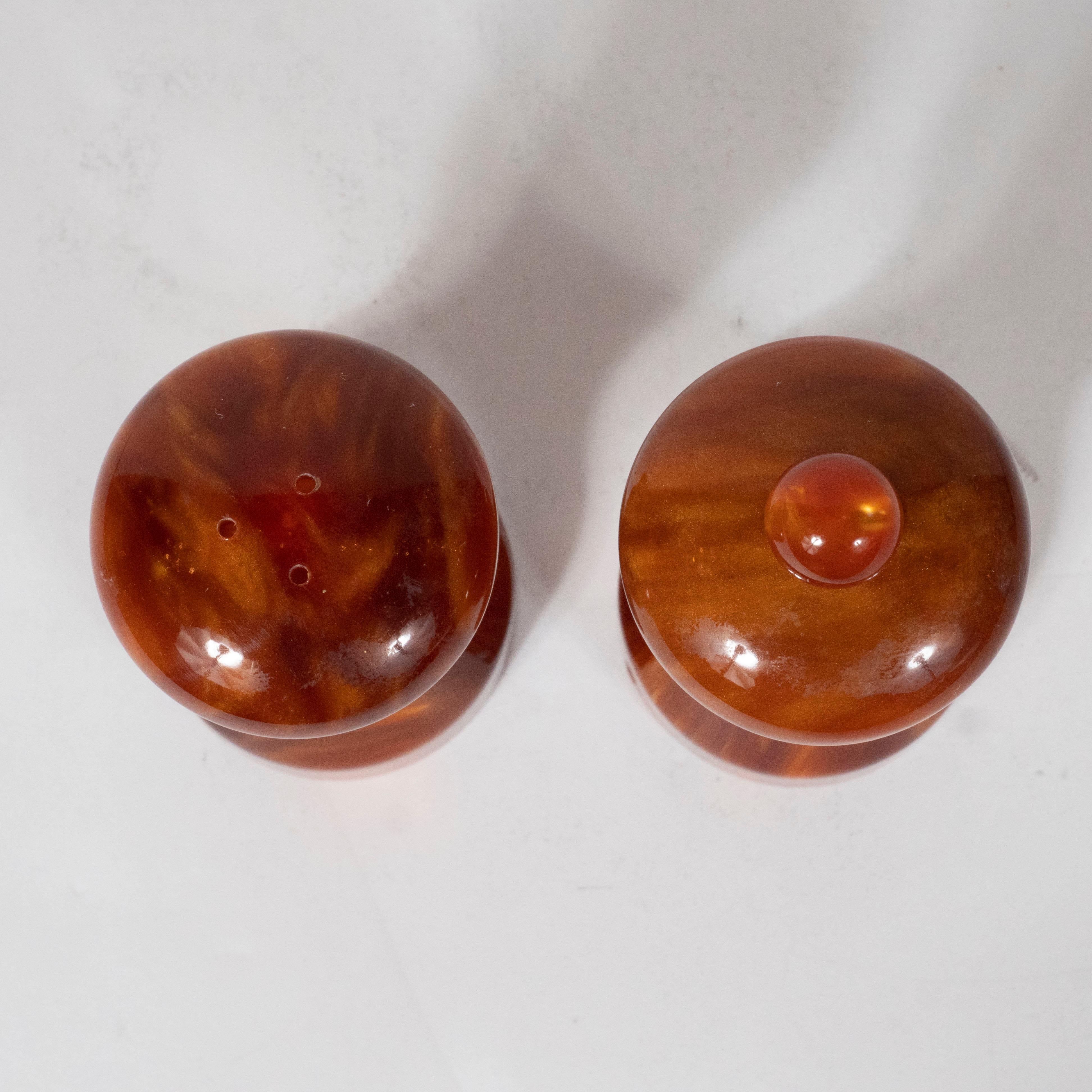 This elegant Mid-Century Modern salt and pepper Shaker set were realized in France circa 1960 by the esteemed maker Au Bain Marie. They feature sinuously curved bodies realized in a mottled tortoiseshell bakelite offering honeyed and amber tones.