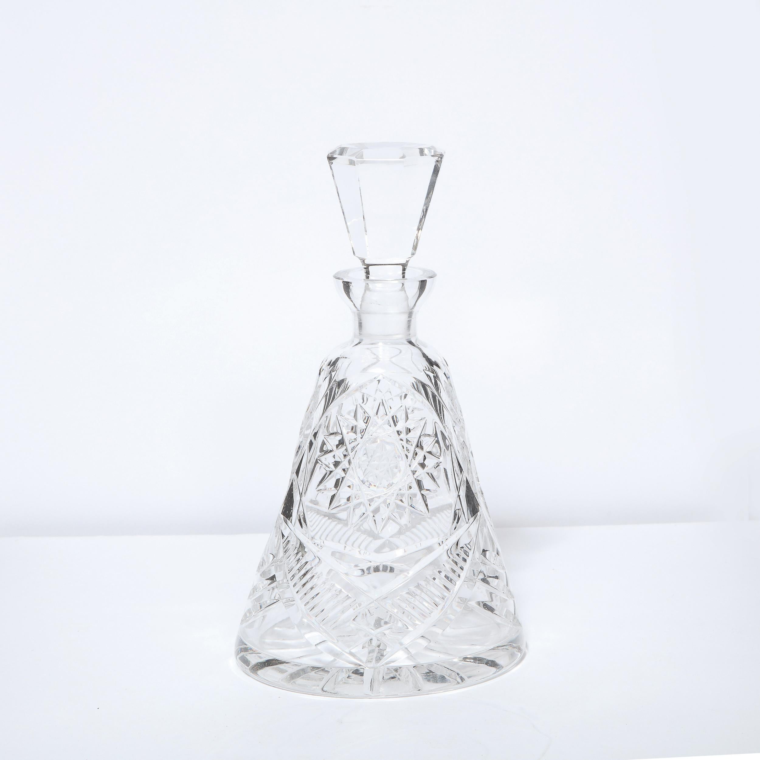 This stunning Mid-Century Modern crystal decanter was realized in the United States circa 1960. It features a conical body in translucent crystal with a wealth of geometric patterns including starbursts and ovoid forms etched into body.