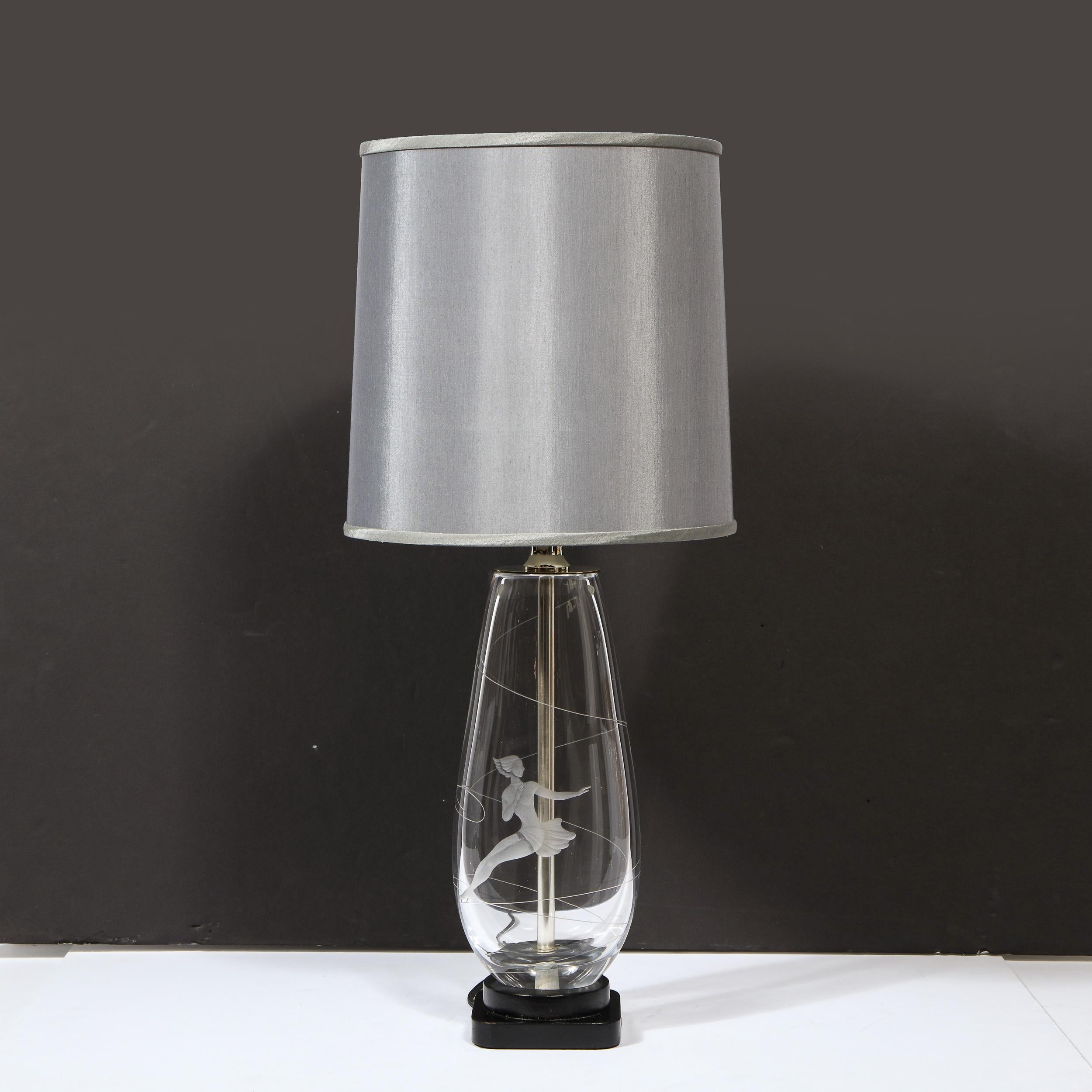 This elegant Mid-Century Modern table lamp was realized by the legendary maker Orrefors in Sweden, circa 1950. It features a cylindrical translucent glass body that tapers at its top sitting on a tiered square black enamel base with rounded edges.