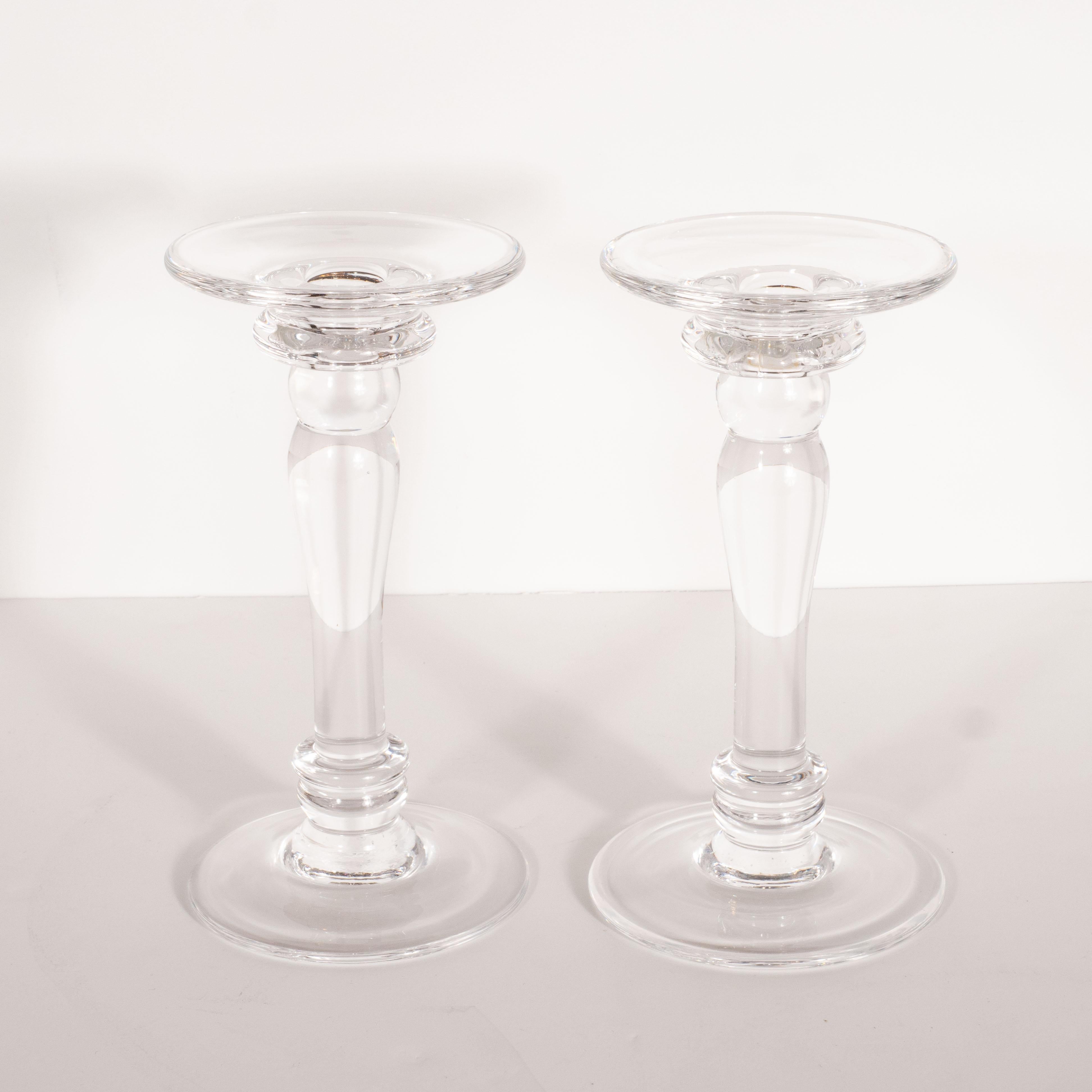 This elegant pair of Mid-Century Modern candlesticks was realized in the United States, circa 1960. Modeled after the Doric columns of ancient Greece, the piece offers a circular base and bobeche, a sinuously curved body with raised banded detailing