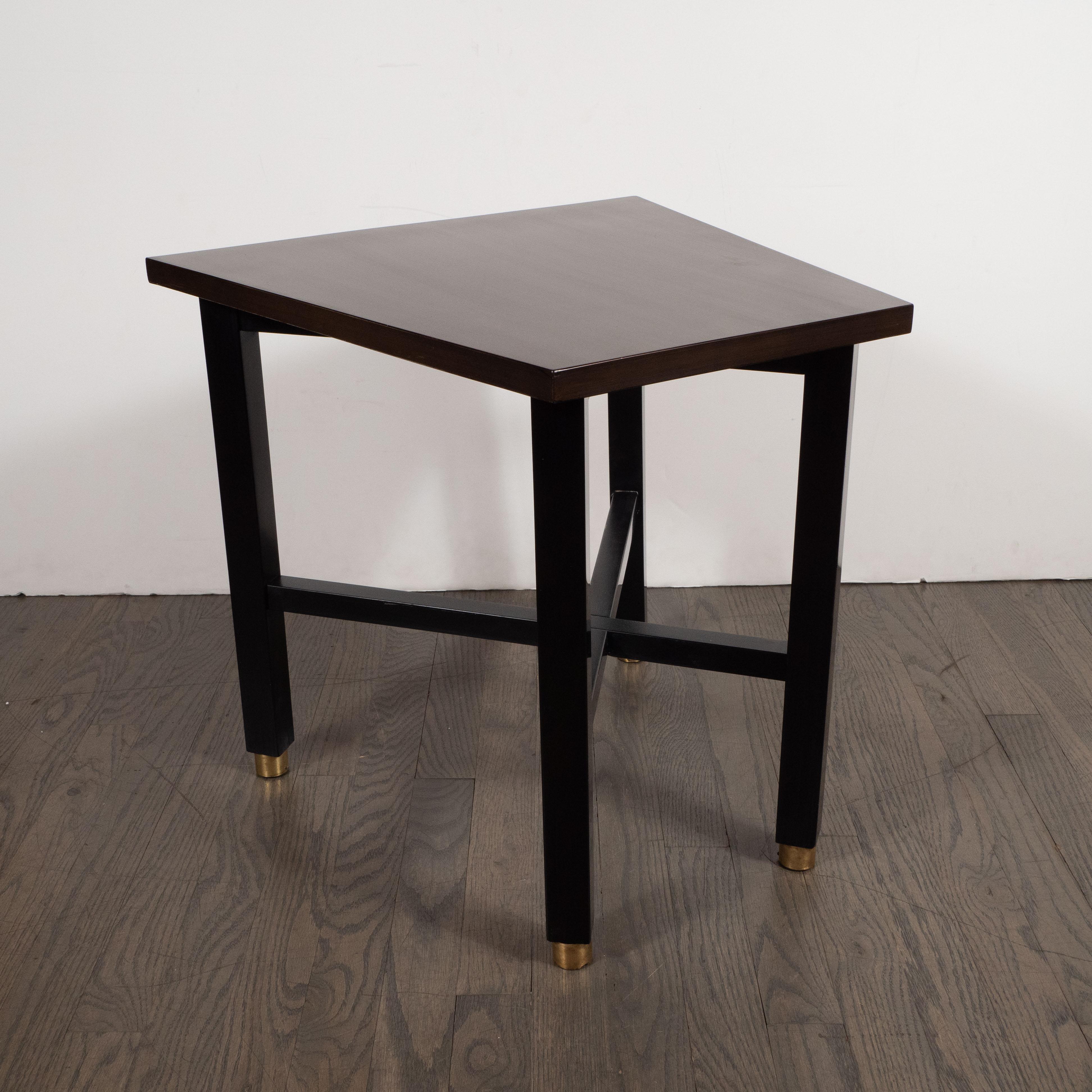 Designed by Dunbar and handcrafted in Berne, Indiana, this elegant side table was realized in the United States circa 1950. Featuring a hand rubbed walnut trapezoidal top and ebonized rectangular legs that sit on brass sabots, this piece is a study
