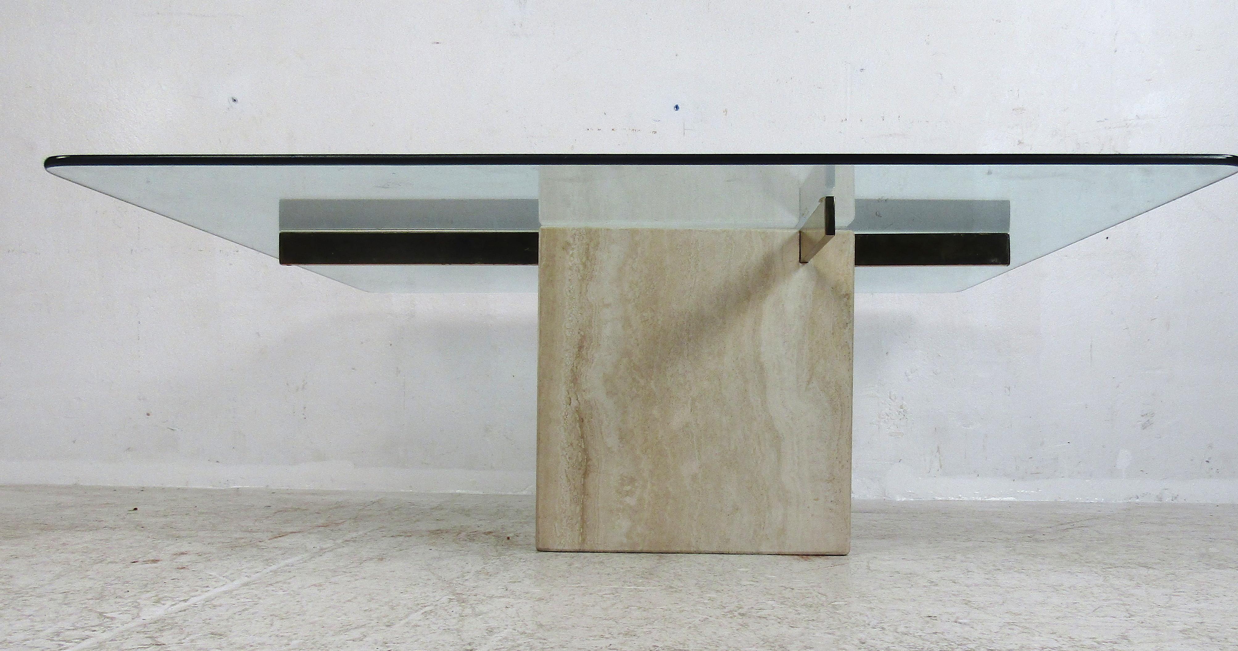 This stunning vintage modern Artedi coffee table features a thick square glass top with a travertine base. Sleek design with two brass supports fitted inside the travertine base holds the large glass tabletop. This elegant piece makes the perfect