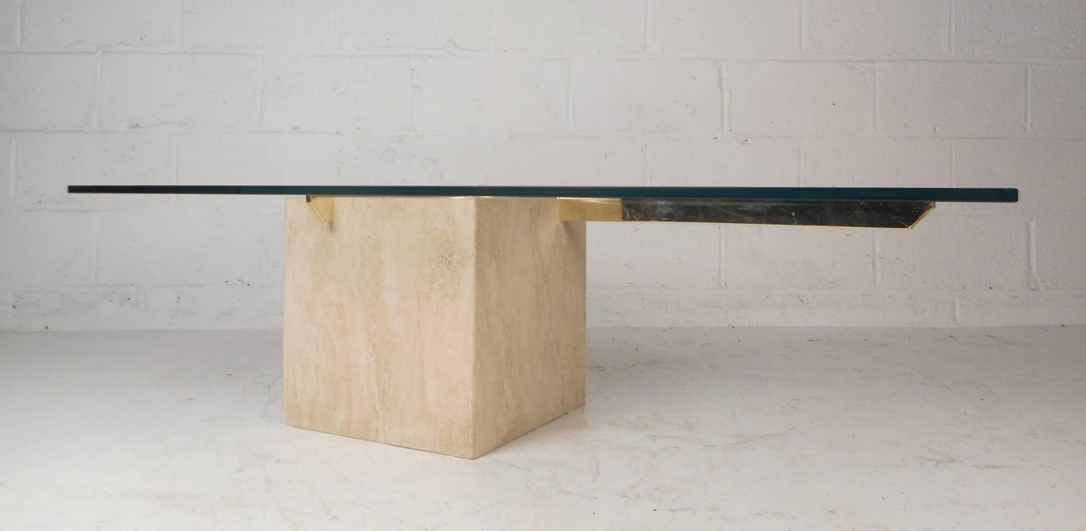 This stunning vintage modern coffee table features a thick rectangular glass top and a cube shaped travertine base. Sleek design with two brass supports fitted inside the travertine base holding the large glass tabletop up. This elegant piece makes