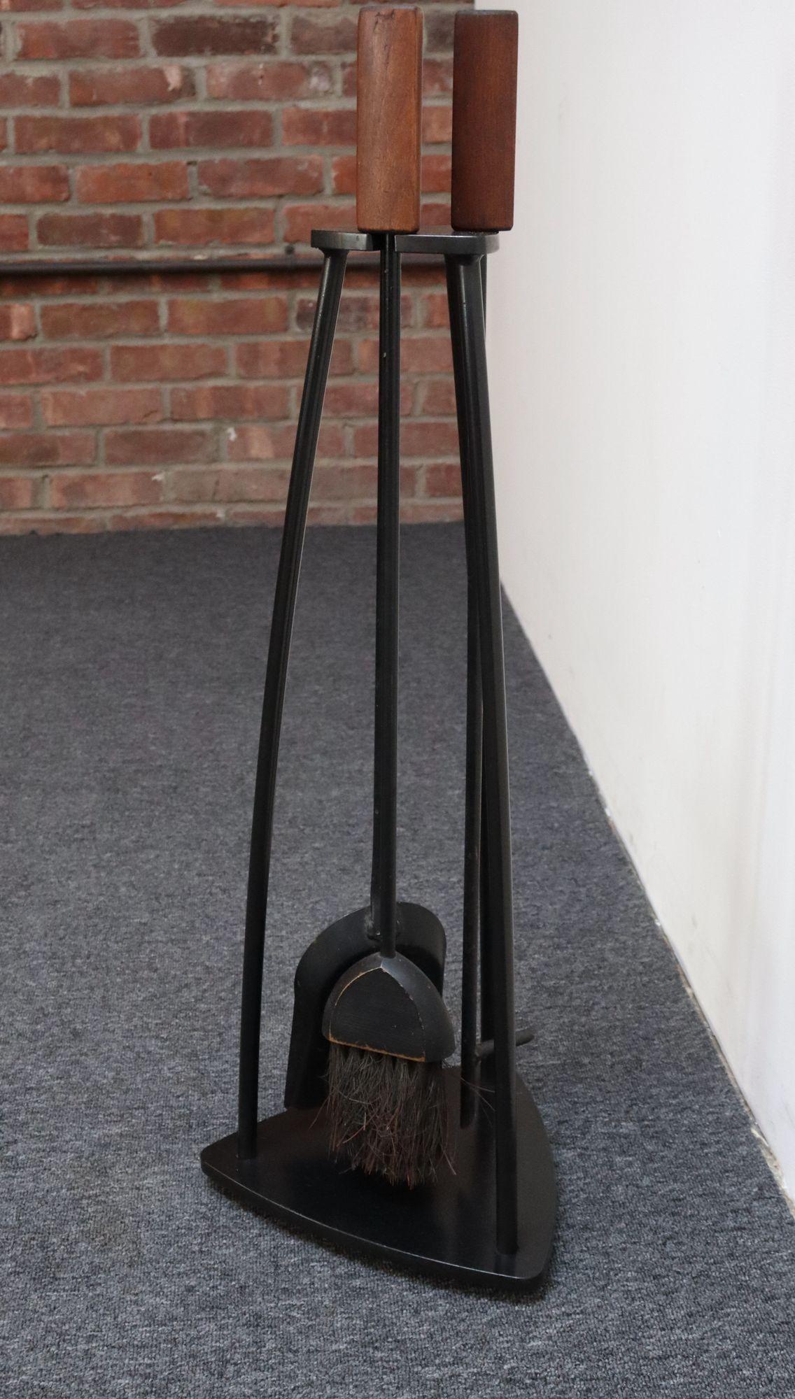 Hand forged iron fire tool set including holder, shovel, brush, and poker (ca. 1960s, USA).
Geometric design elements present - bent iron rod frame connecting a guitar pick-form base and corresponding cradle with tools boasting dense, triangular,