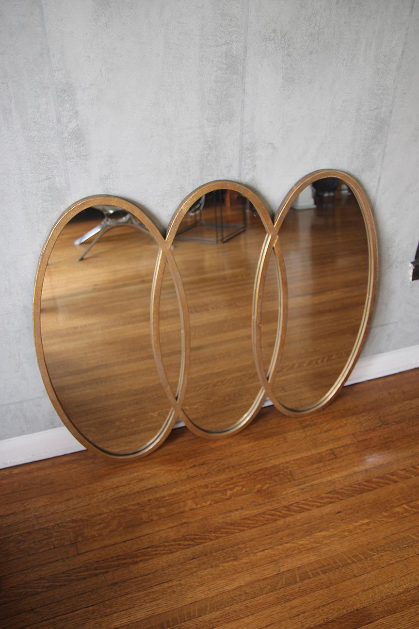 Introducing a stunning trio of interlocking oval mirrors that serve as both functional pieces and works of art. Adorned with intricate rustic gold leafing, they reflect light warmly, adding vintage charm to any room. 

Showcasing mid-century design,