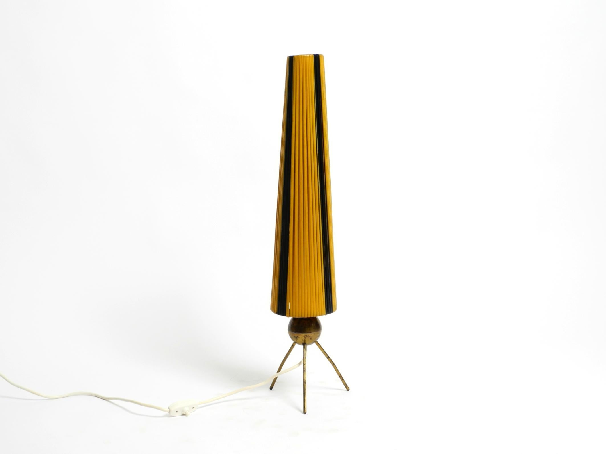 Très rare, belle lampe de table à trois pieds en laiton de style moderne du milieu du siècle.
L'abat-jour original est constitué de bandes de nylon jaune et noir enroulées.
Un grand design minimaliste typique des années 1950.
Les pieds sont