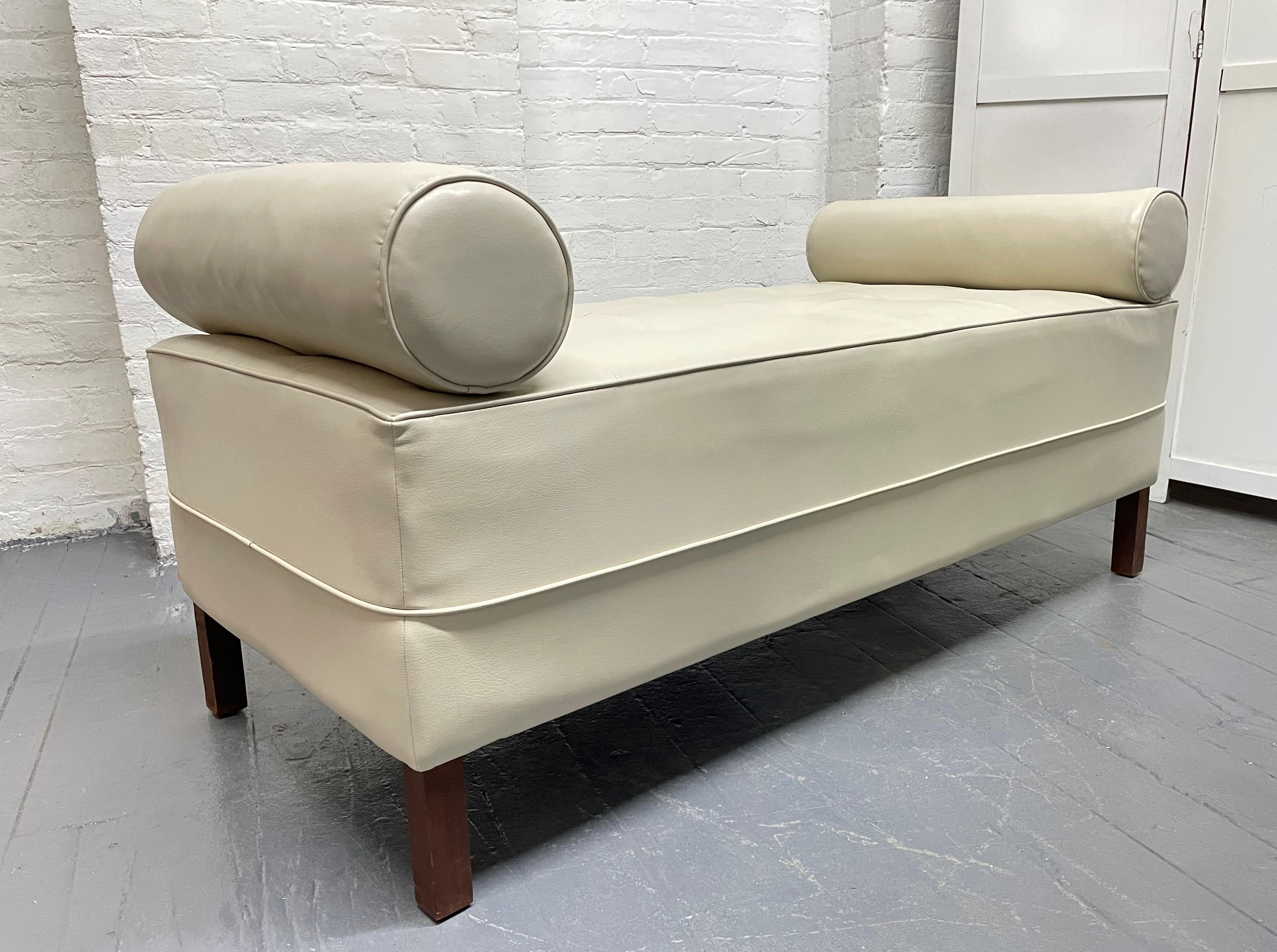 Mid-Century Modern tufted bench. The bench is newly upholstered in leatherette has solid wooden legs and two attached cylindrical shaped pillows.