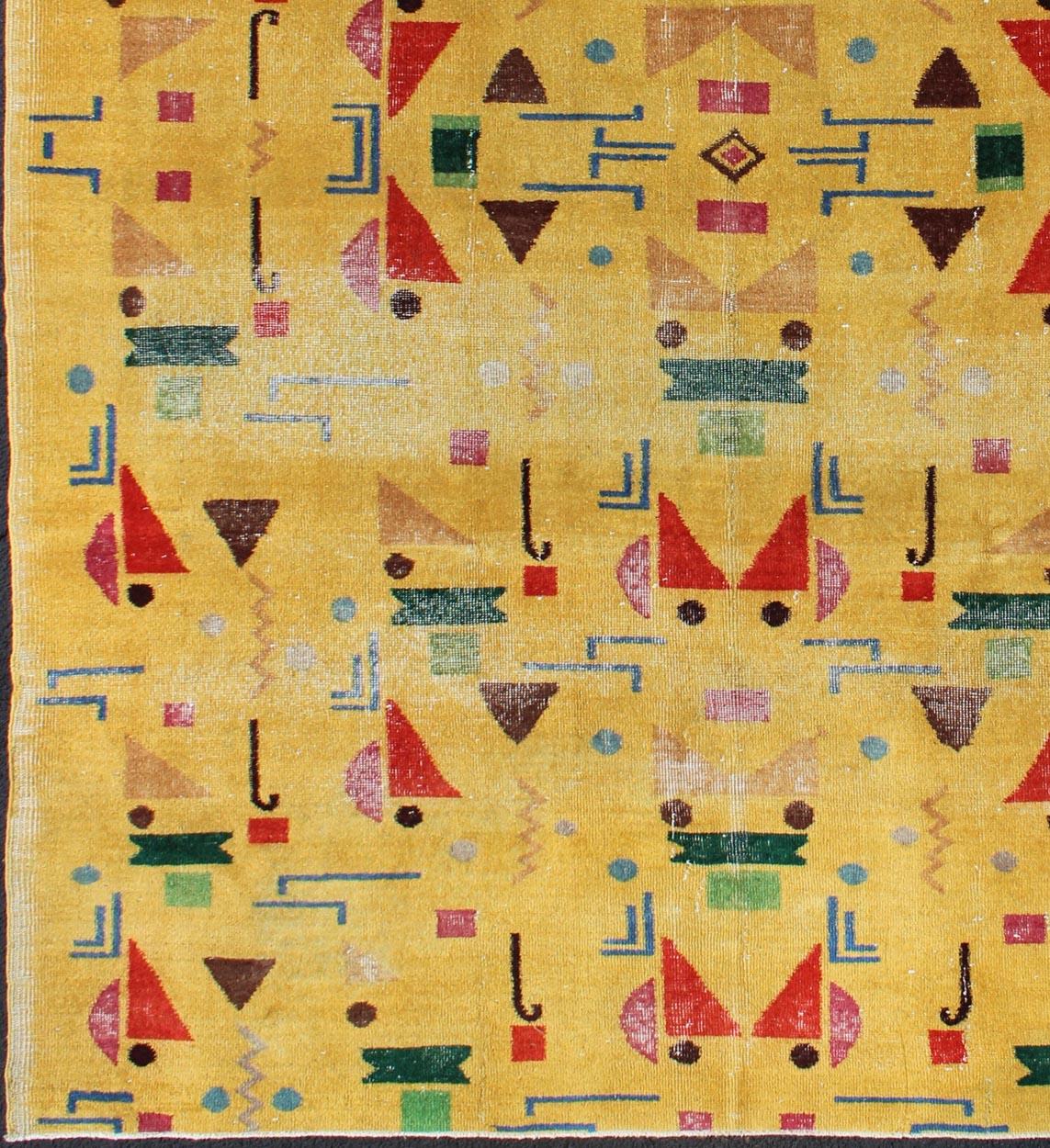 Ce tapis moderne du milieu du siècle finement composé présente un motif géométrique symétrique aux formes variées, composé de nuances vives de jaune, rouge, vert, bleu et marron, faisant de ce tapis une excellente option pour les intérieurs