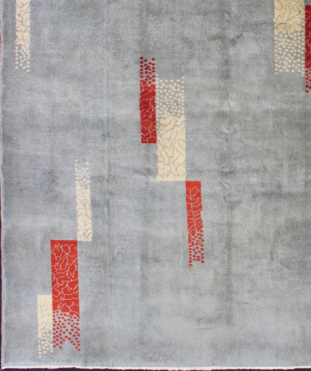 Rendered in box shapes with a spotted and speckled assortment of rich red and cream colors, this very unique Mid-Century Modern rug has an abstract design set on a pale gray-blue background making it a great fit for a variety of modern and