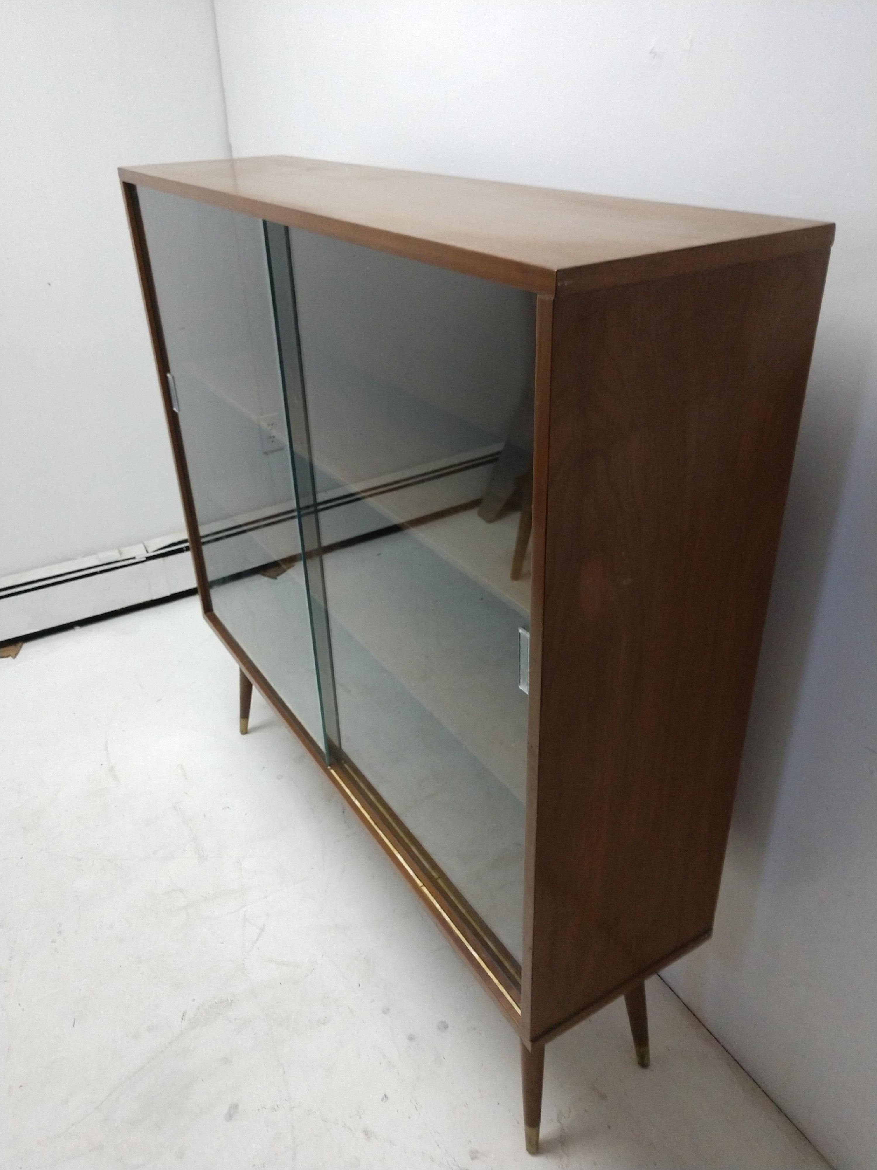 Large midcentury bookcase on splayed legs. Created out of walnut, has two sliding glass doors. In excellent vintage condition. Two adjustable shelves.