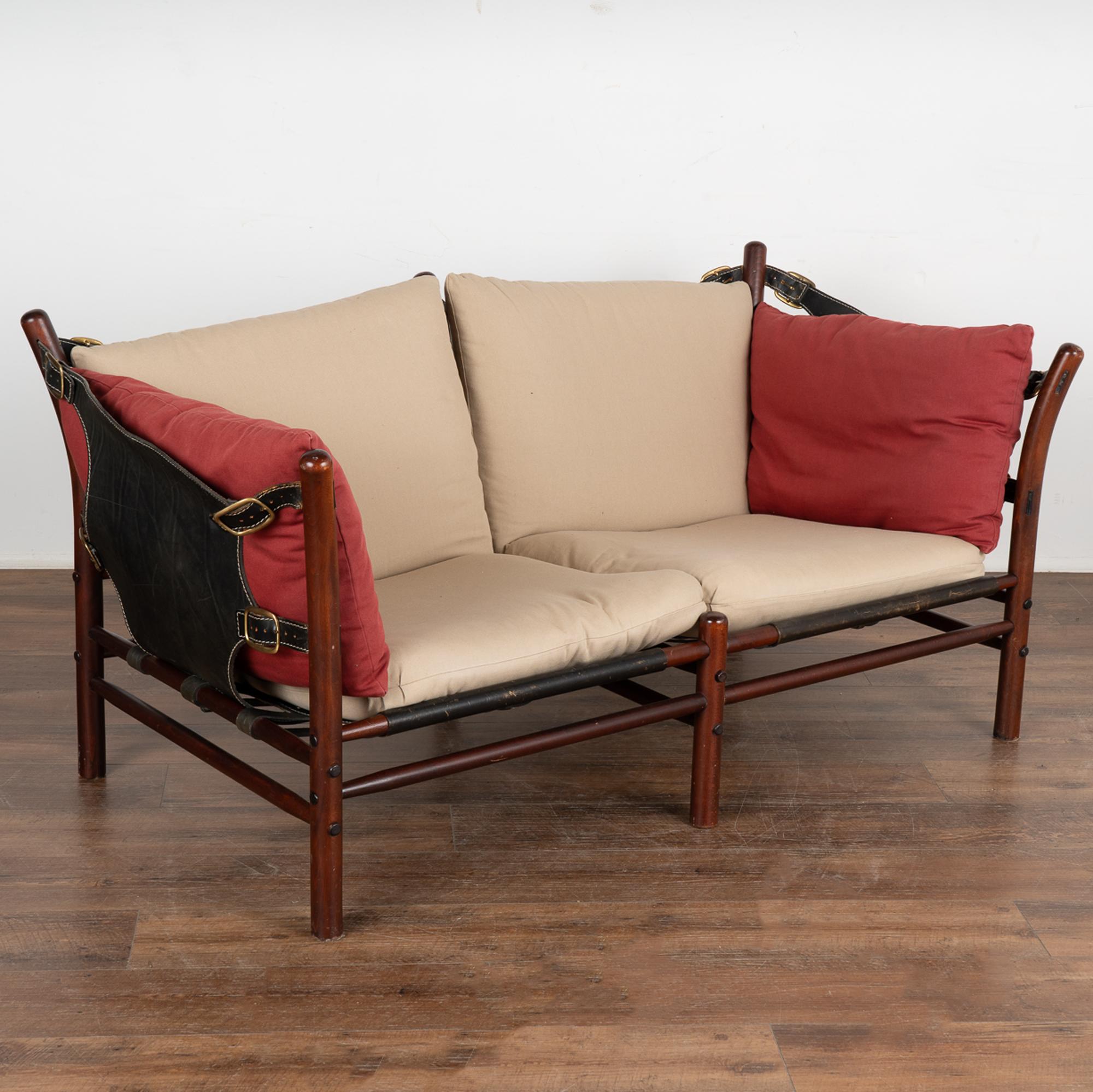Mid-Century Modern two-person sofa designed by Arne Norell. Leather sling sides and back, loose cushions are covered in neutral and contrasting brick red fabric. The Illona model was inspired by safari furniture and manufactured by Aneby