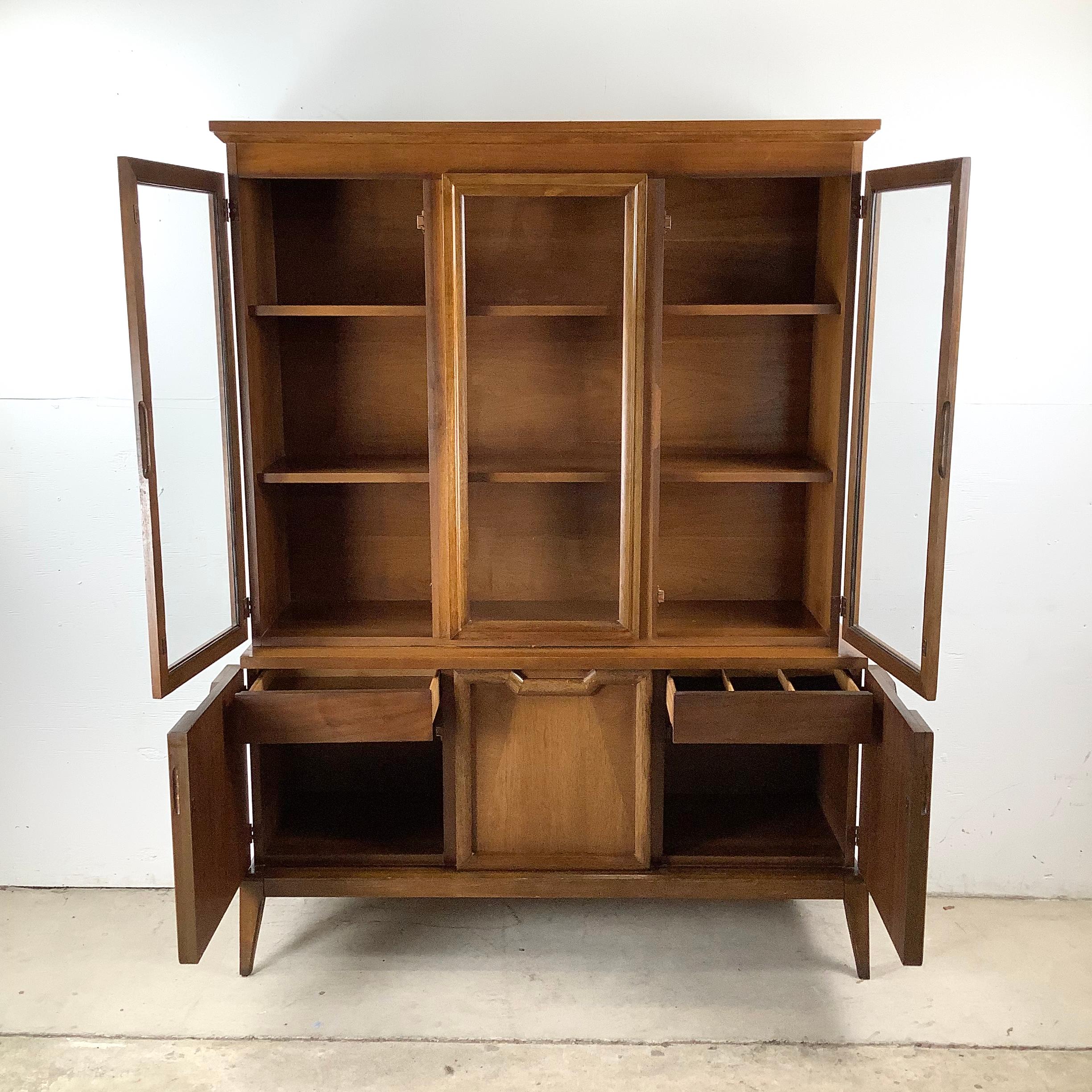 Este mueble de porcelana de nogal de mediados de siglo ofrece elegancia y funcionalidad en un diseño compacto. La pieza está dispuesta en dos secciones: un mueble inferior con almacenamiento cerrado y cajones, y una vitrina superior con frente de