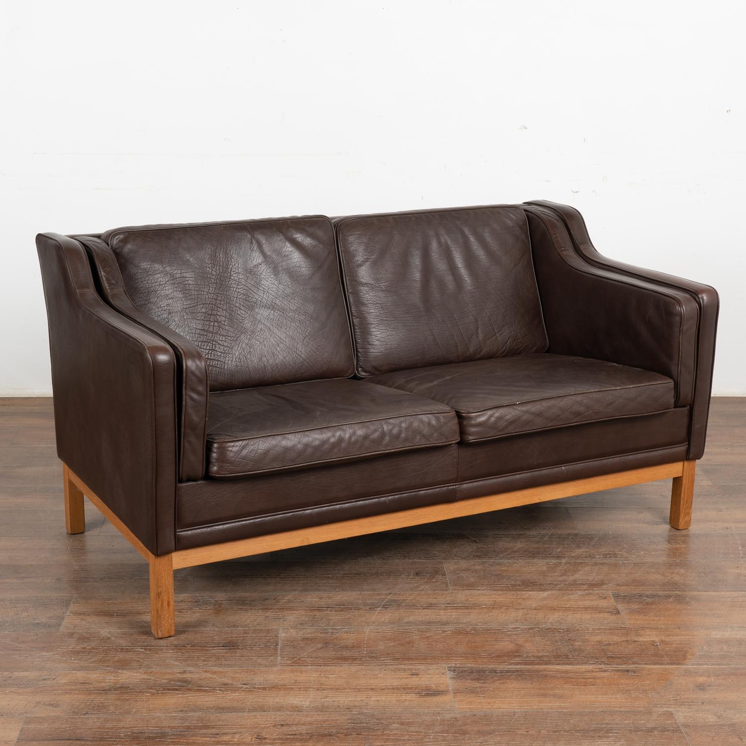 Mid-century modern vintage two seat brown leather sofa or loveseat from Denmark. This comfortable sofa combines tradition with modern lines.
Upholstered in dark brown leather, loose cushions, hardwood legs in stained beech wood. 
Sold in used