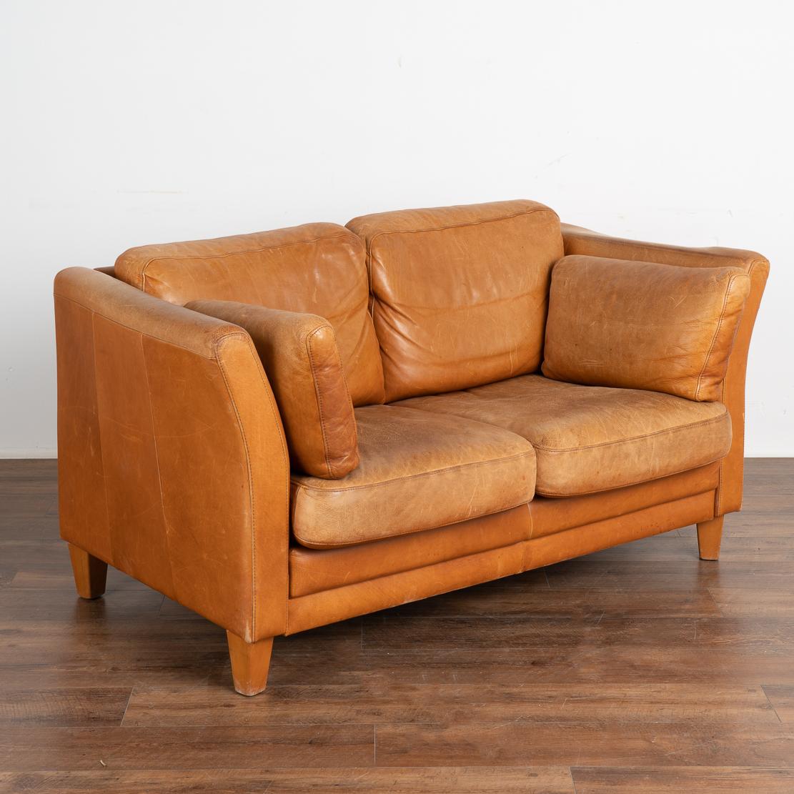 Mid-century modern vintage zwei Sitz Leder Sofa Loveseat. Ein bequemes Sofa, das Tradition und Moderne vereint.
Gepolstert in camel- oder karamellbraunem Leder, lose Kissen, Beine aus gebeiztem Buchenholz. 
Verkauft in gebrauchtem Vintage-Zustand,