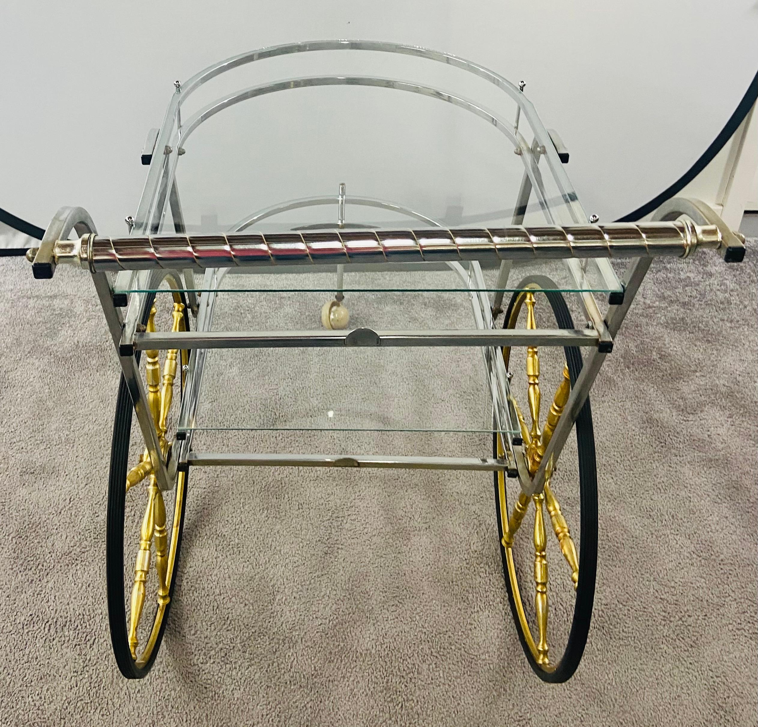 Un élégant chariot de bar ou de service à thé à deux niveaux, de style Mid-Century Modern. Le chariot est doté de grandes roues de style chariot, de deux étagères en verre et d'une roulette avant à boule ronde à roue libre. Ce chariot de service