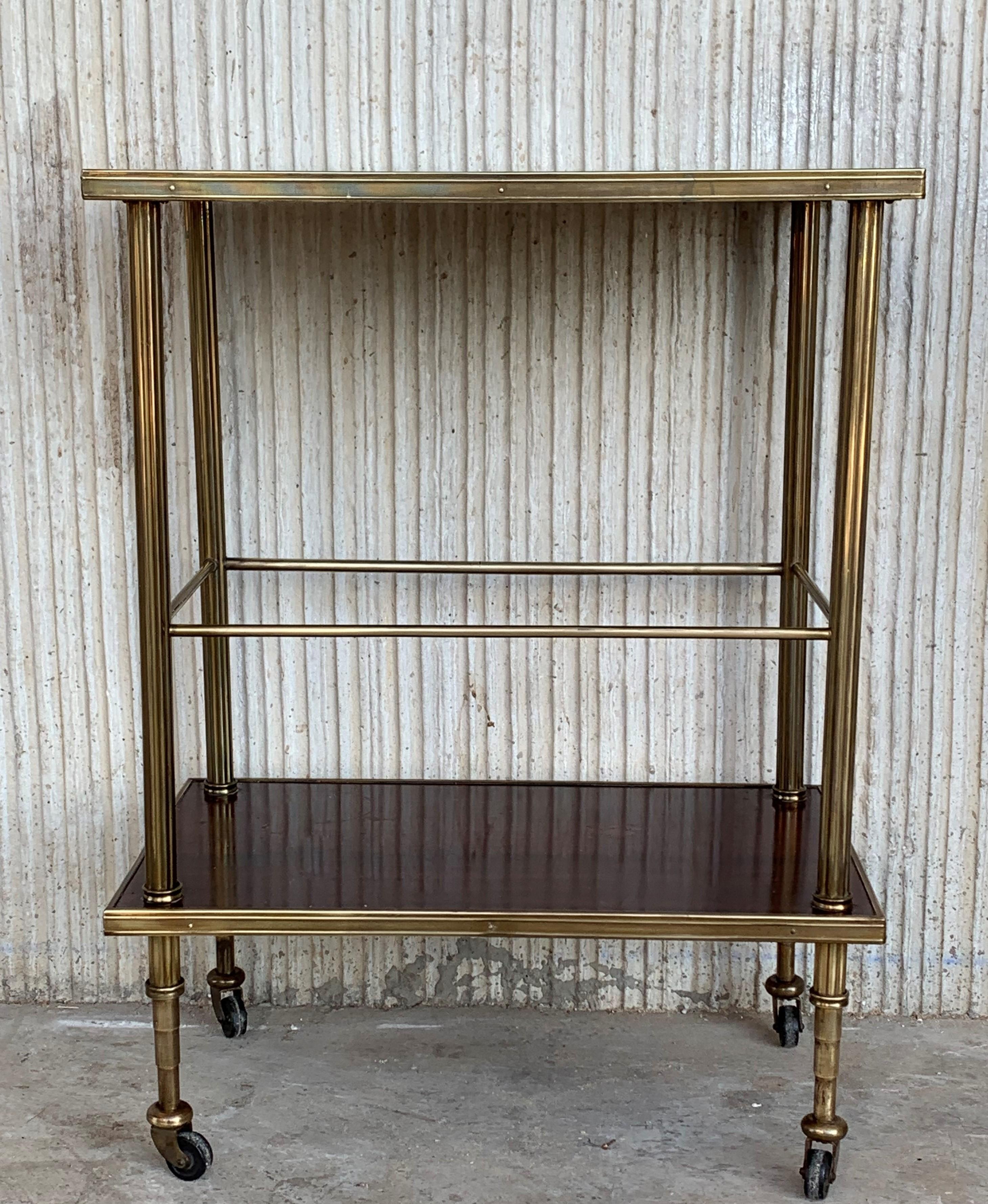 Mid-Century Modern two-tier brass and mahogany veneer glass side table in Maison Jansen style with fluted brass legs and wheels.