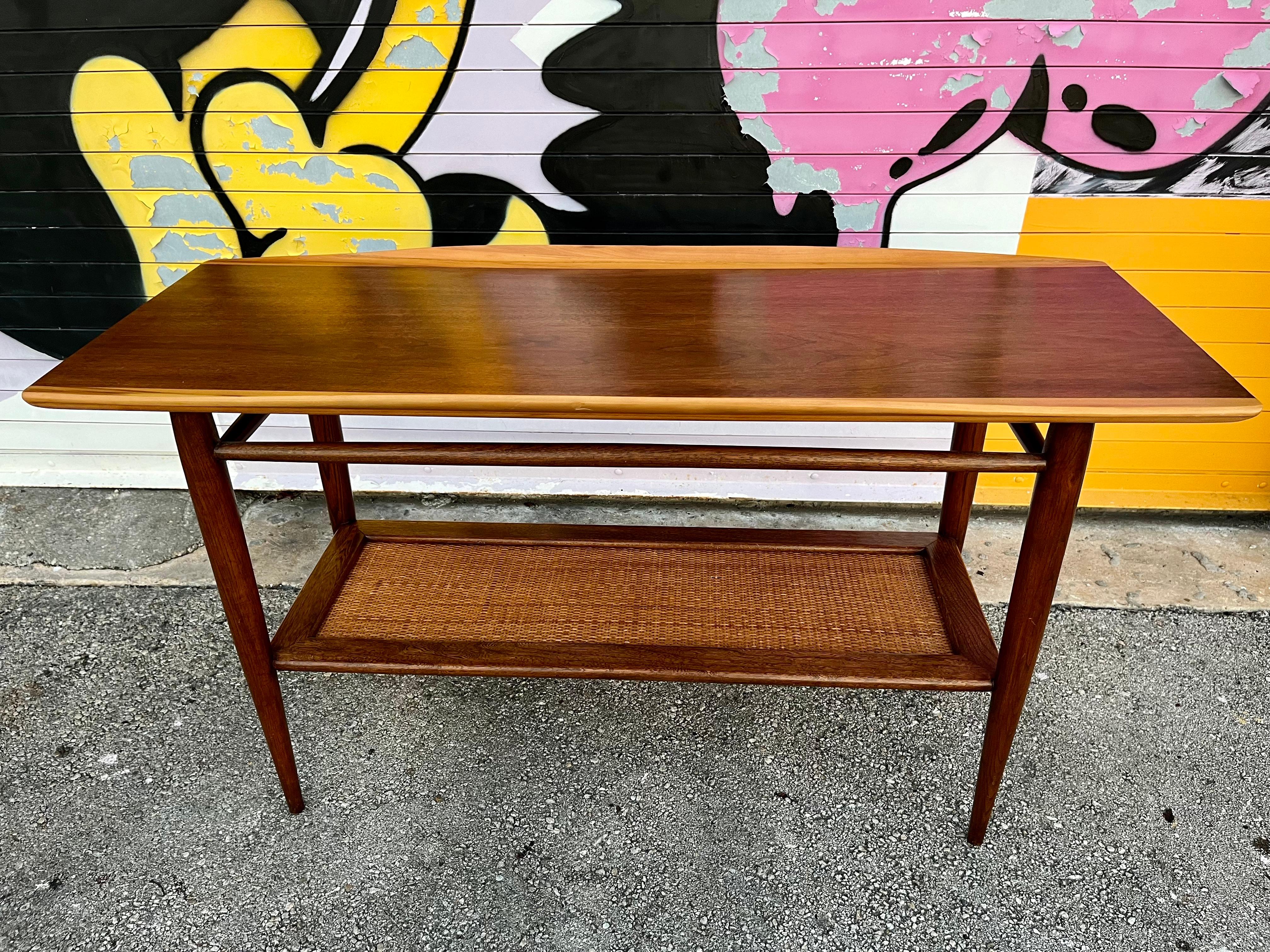 Vintage Mid Century Modern Danish style surfboard two tier Console / Sofa/ Entry Table by Bassett. Circa 1960s.
Features a quintessential MCM Sleek profile with a beautiful wood grain and two tones top  with folded lips and a bottom tier covered
