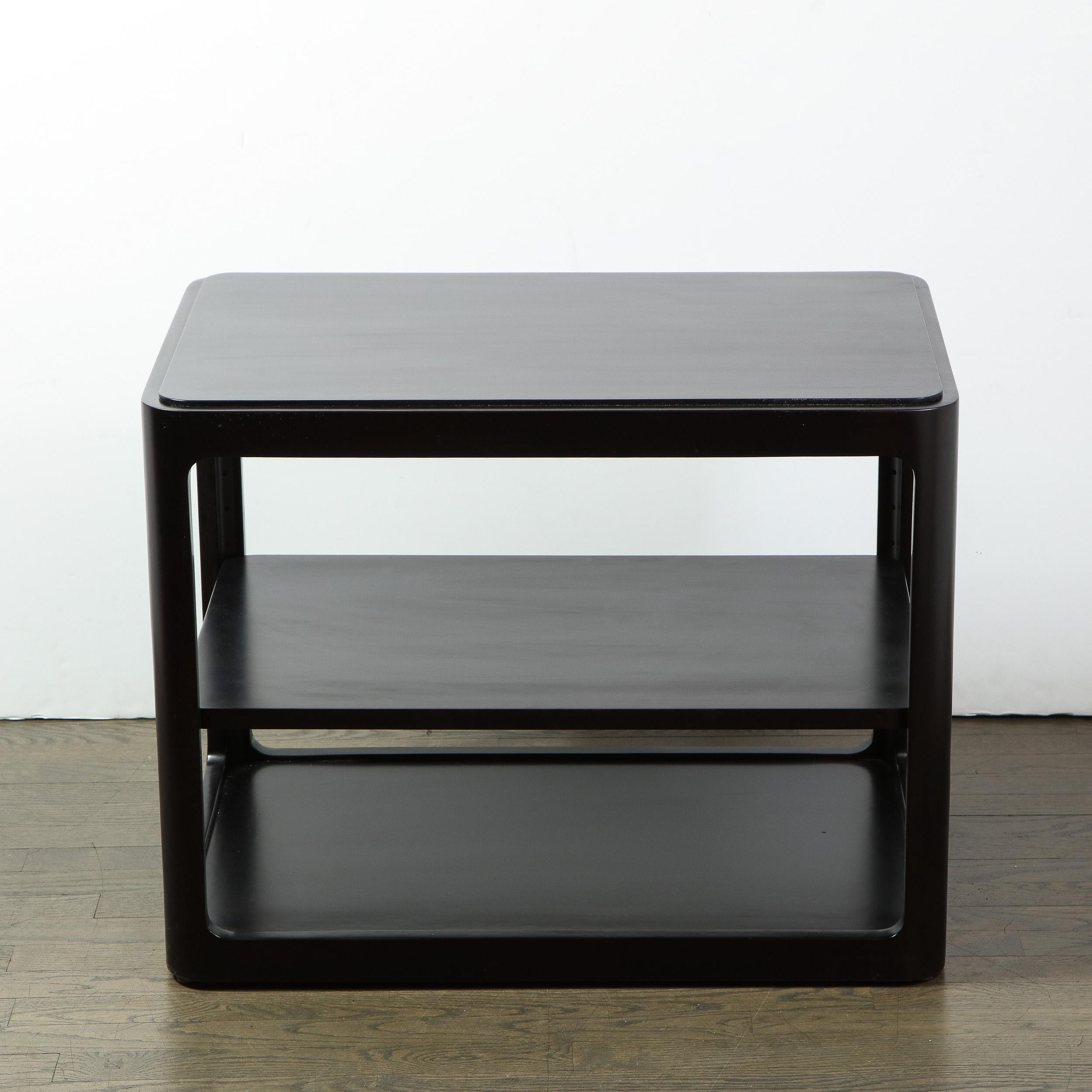 This elegant Mid-Century Modern side/ end table was handcrafted in Berne, Indiana by the fabled American design firm Dunbar, circa 1960. It features a two-tier rectangular form with rounded corners and a subtly inset top- all finished in ebonized
