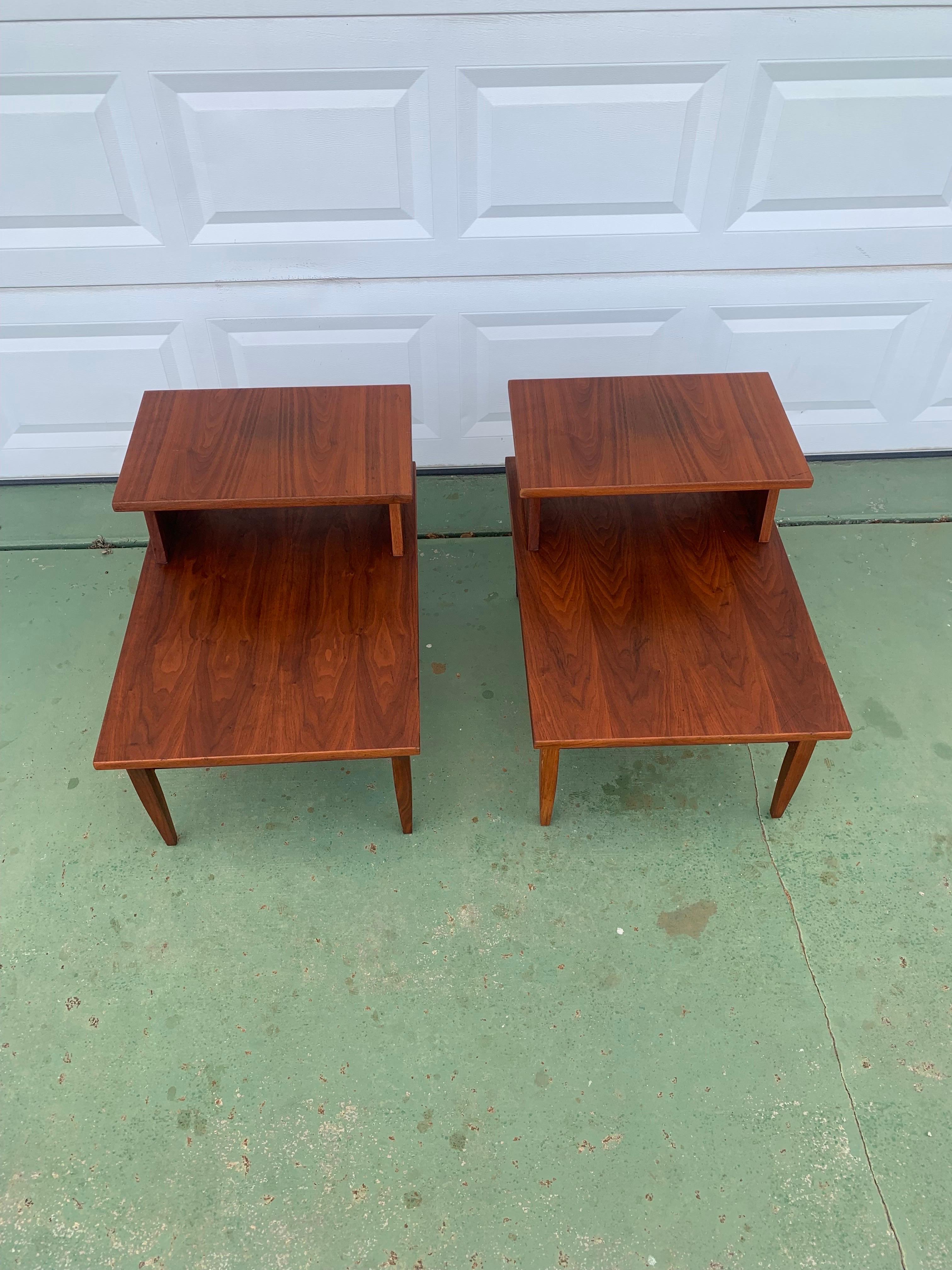Beautiful pair of Mid-Century Modern two tiered end tables. Recently refinished walnut with brass accents. Beautiful grain pops as it flows from one end of the table to the other. The tables also have a magazine rack on the below the main table top.