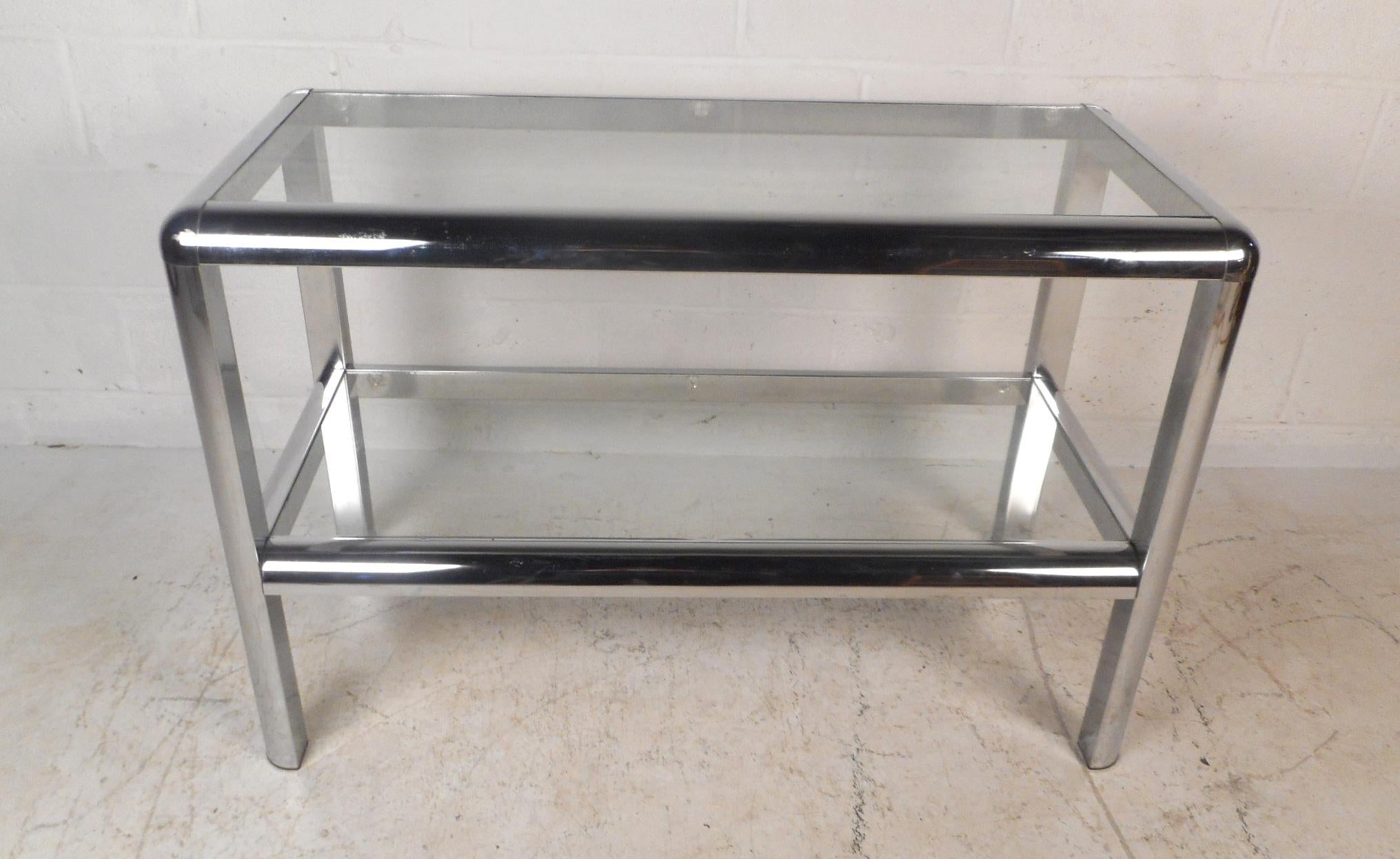This stunning vintage modern console table features two tiers of glass shelving within a tubular metal frame. A unique and versatile design that can function as an end table, coffee table, or a console table. This sleek midcentury piece makes the