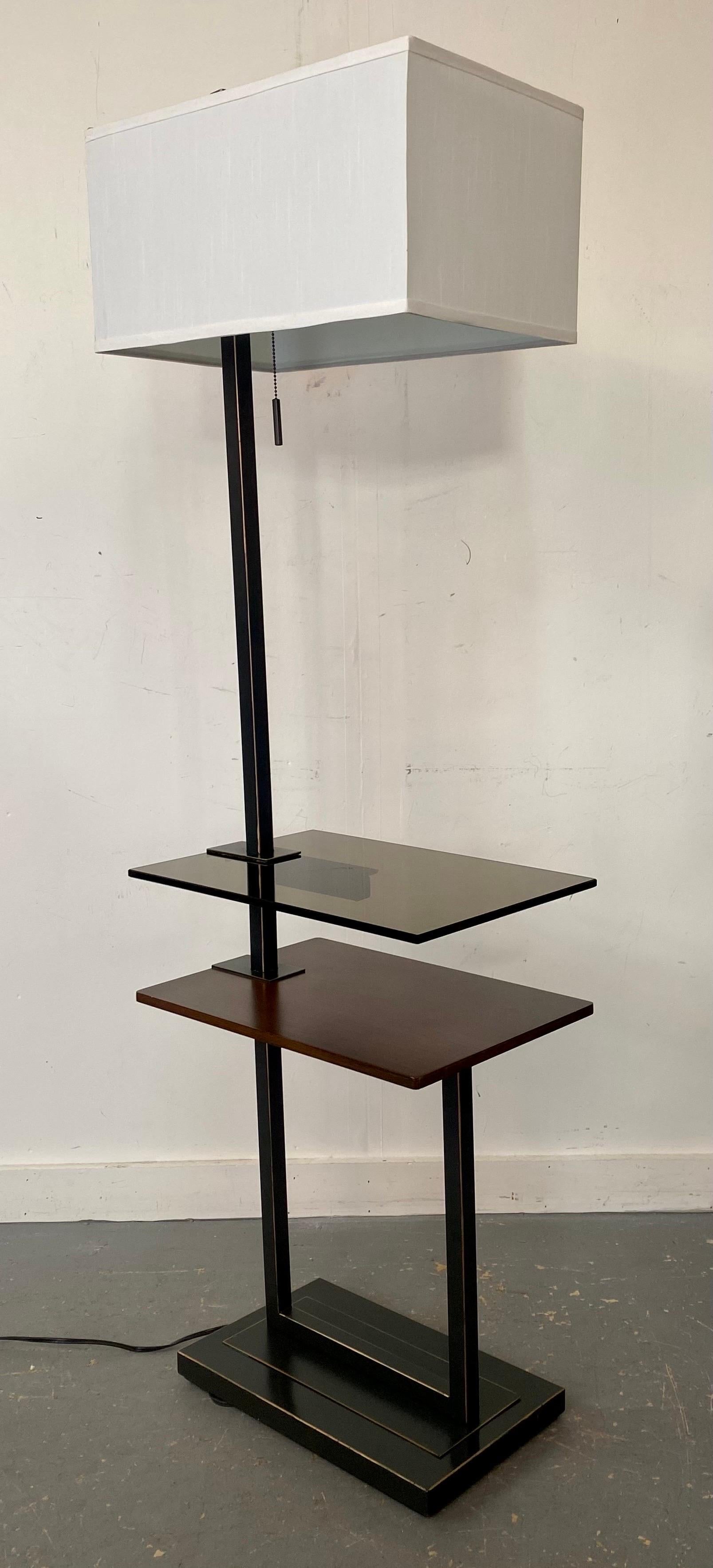 A quality Mid-Century Modern two-tier table floor lamp. The Black framed floor lamp features a rectangular base holding one cherry wood table / tray. The second shelf / tray is made of thick fiberglass tinted in brown to match the wooden table. The