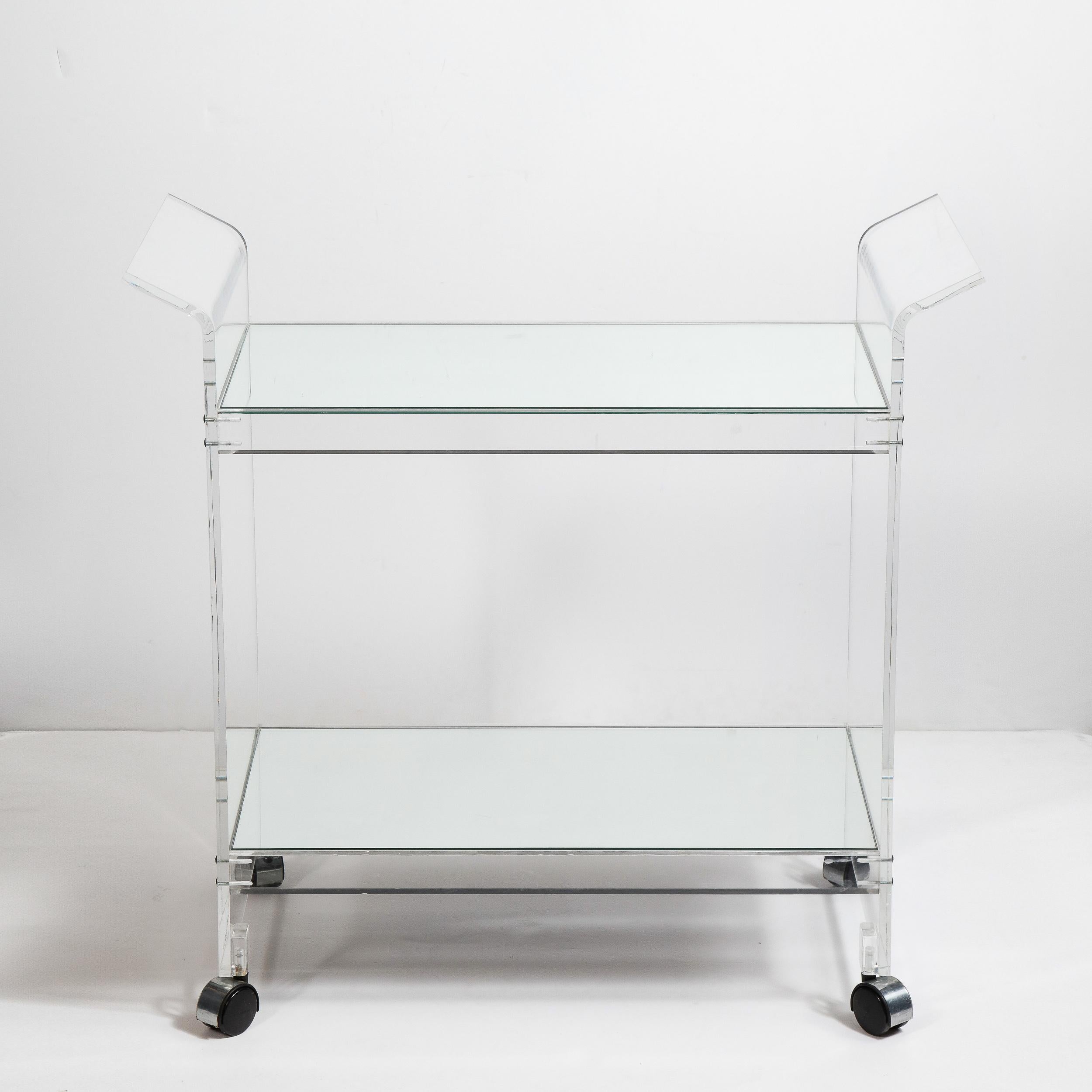 This chic and refined Mid-Century Modern bar cart was realized in the United States, circa 1970. Fabricated in translucent Lucite and sitting on chrome wrapped castors, this piece consists of two side supports with stylized wing detailing at their