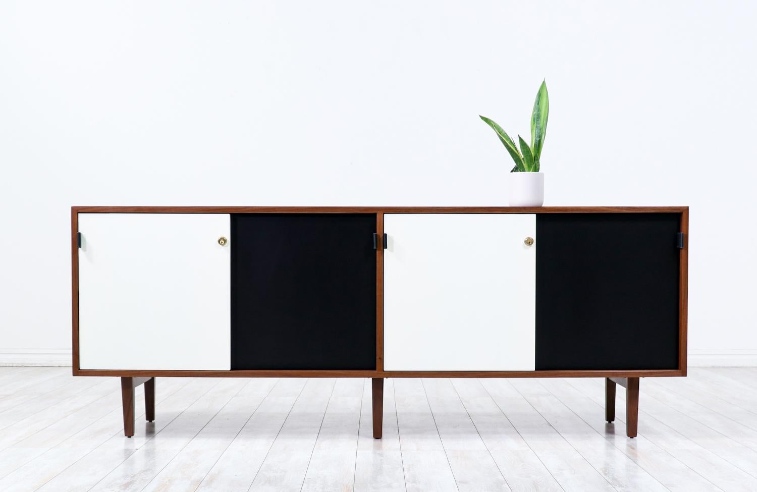 Elegant credenza designed by architect and designer Florence Knoll and manufactured by Knoll Associates Inc, circa 1950s. This iconic design features a walnut wood case over six solid walnut legs. Four offset black and white lacquered sliding doors,